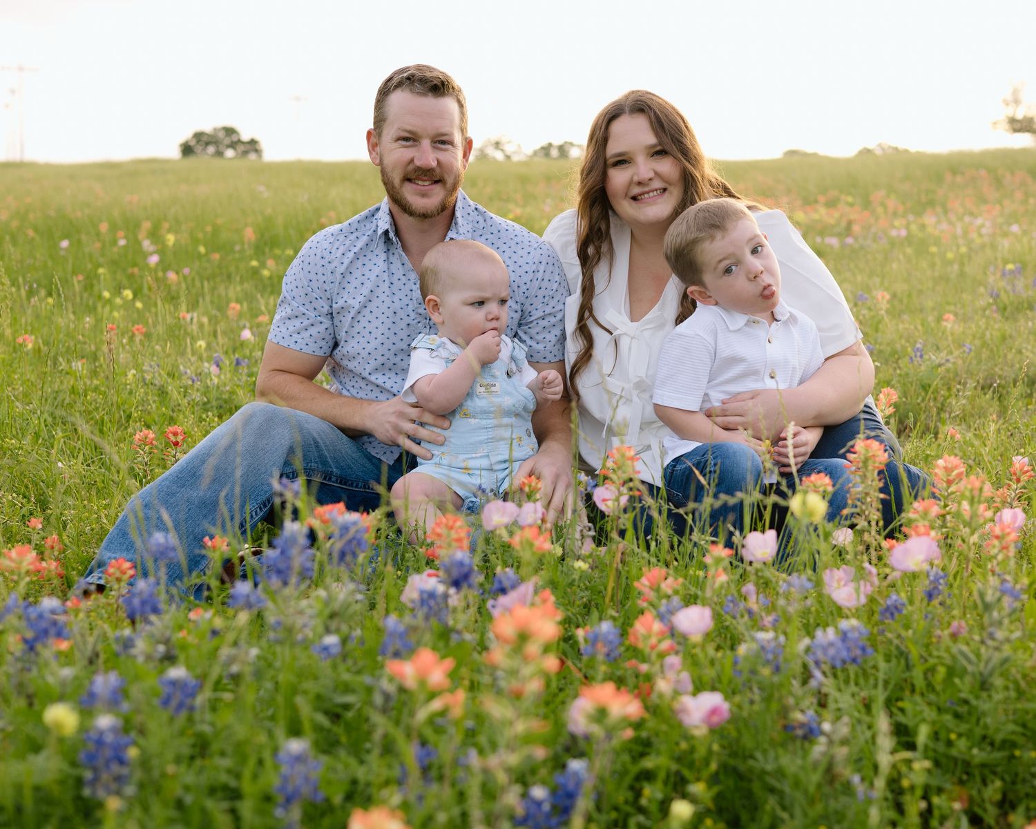 A family sits together in a vibrant wildflower meadow filled with bluebonnets and other colorful Texas wildflowers.