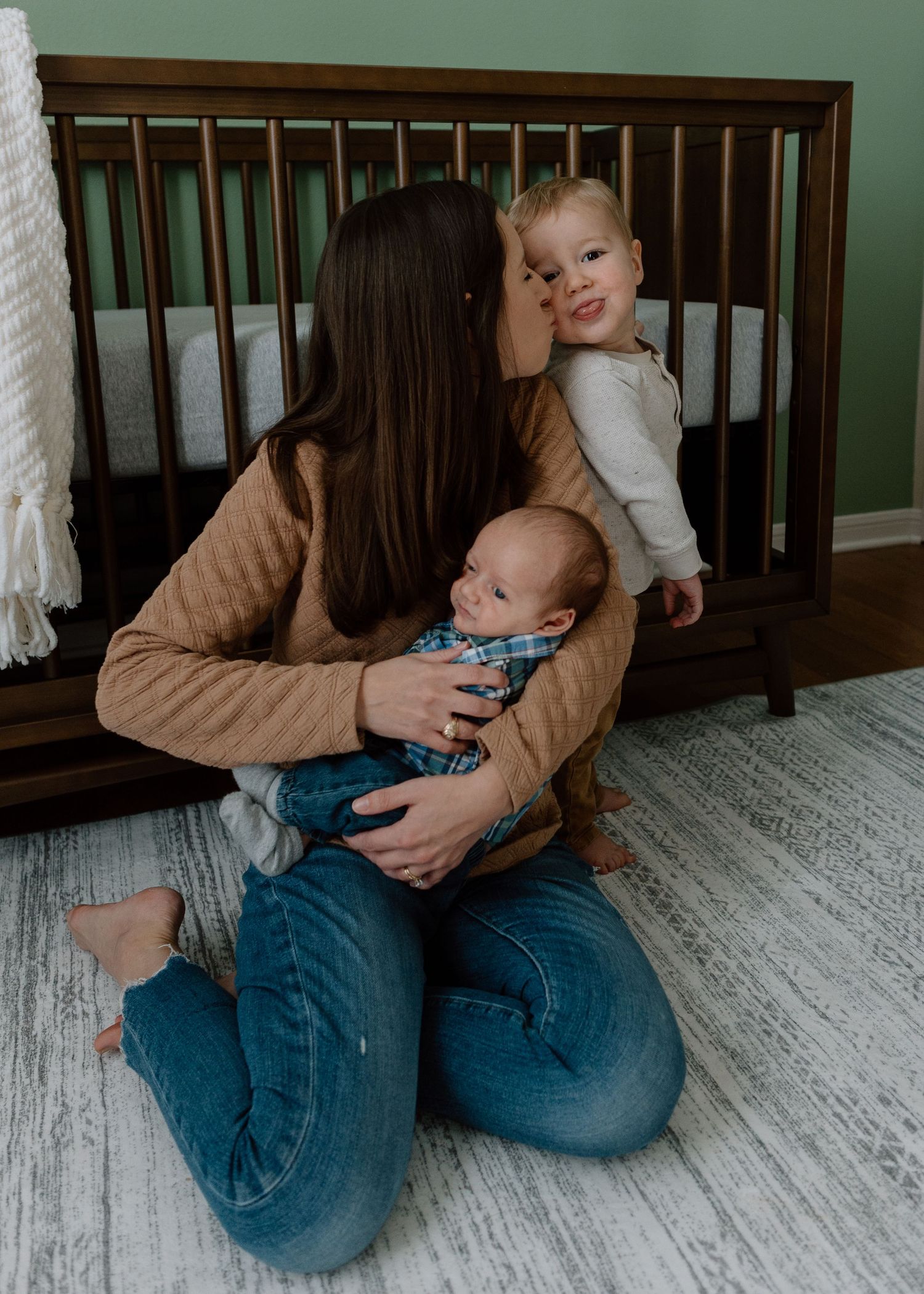 Sweet family moment captured in a nursery with a wooden crib, green walls and light flooring.