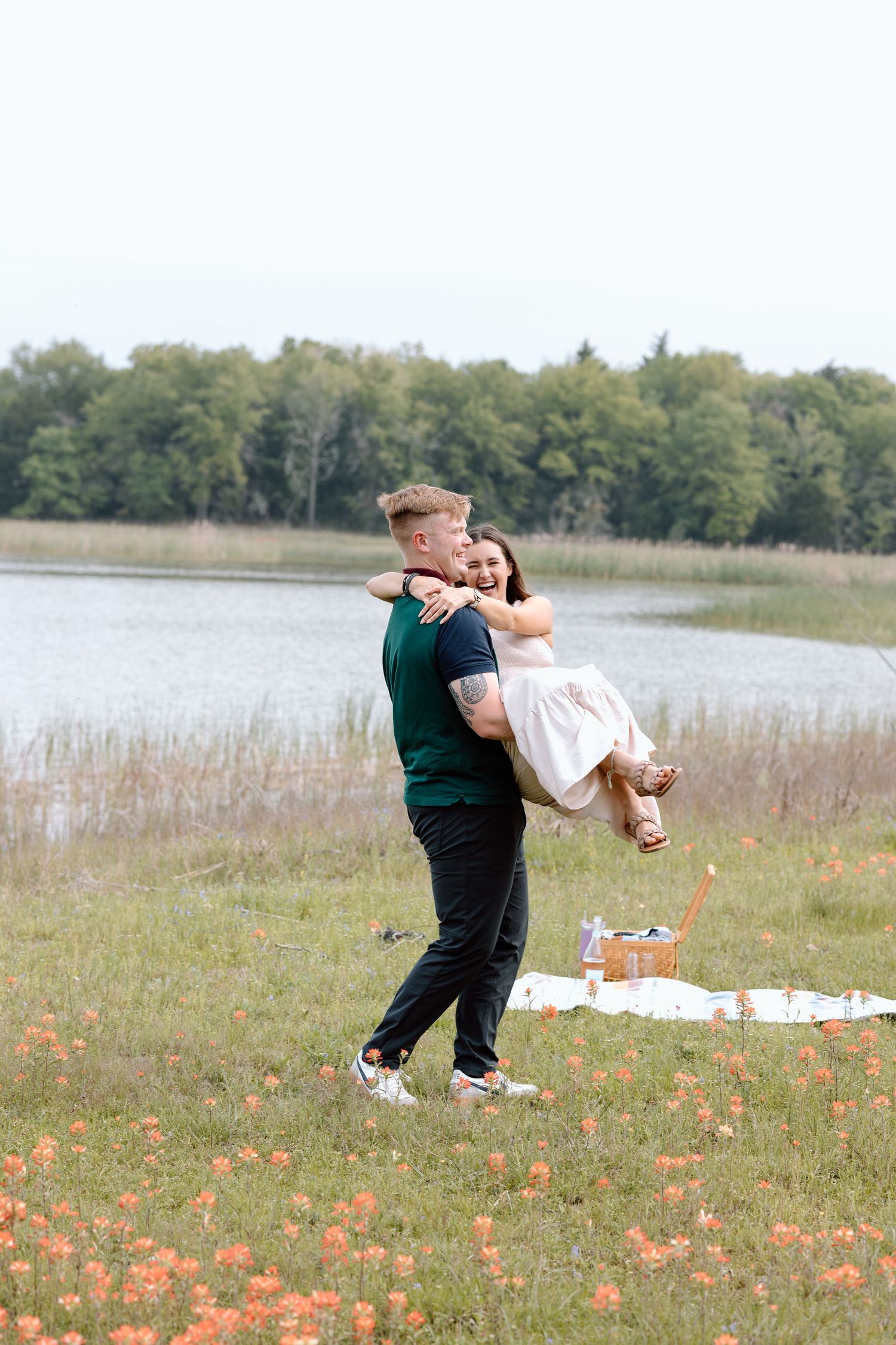 A couple enjoys a spirited moment during a lakeside picnic with wildflowers.