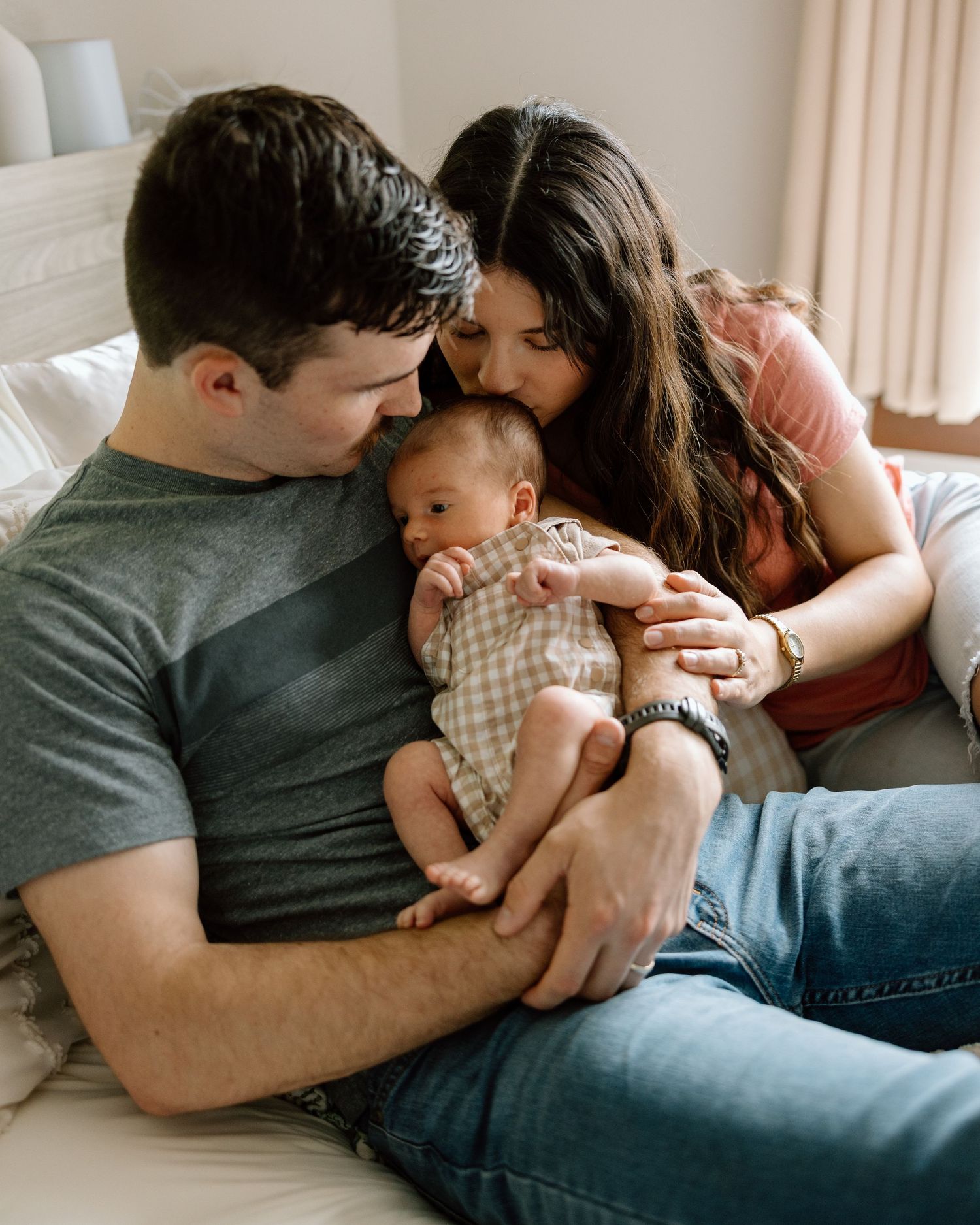 Parents lovingly cradling their newborn baby on a bed, mother kissing infant's head.