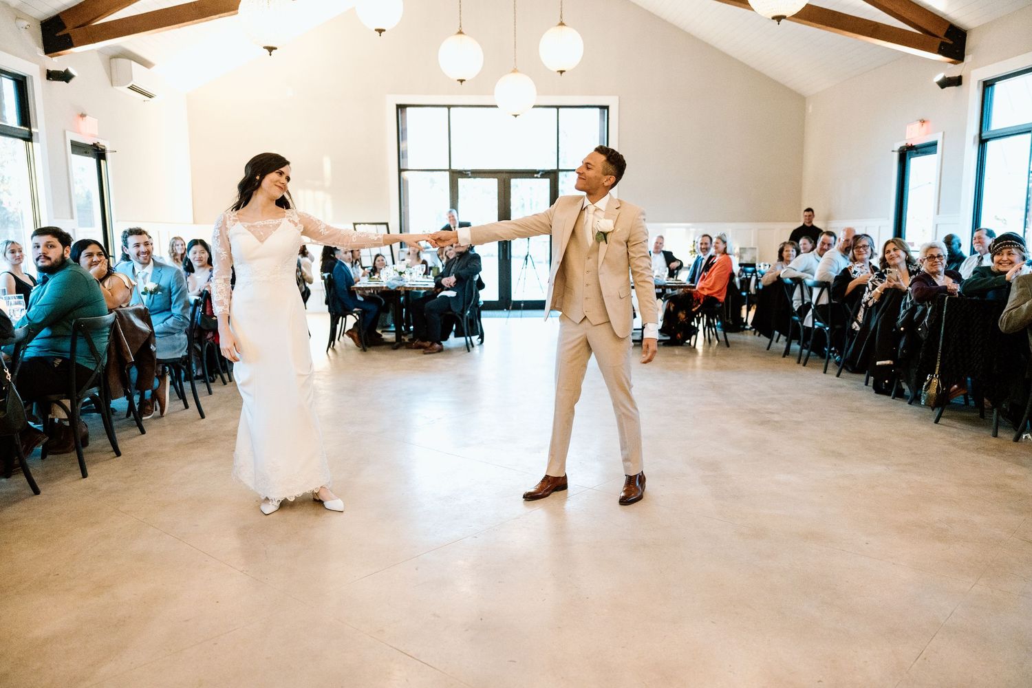 Bride and groom sharing first dance at wedding reception with guests seated around.