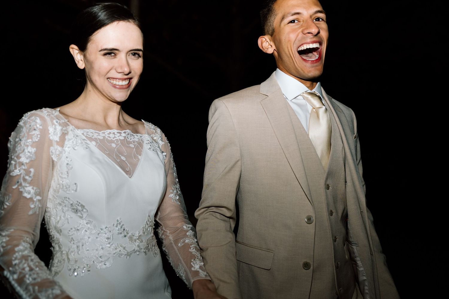 Joyful bride and groom laughing together at wedding reception against dark background.