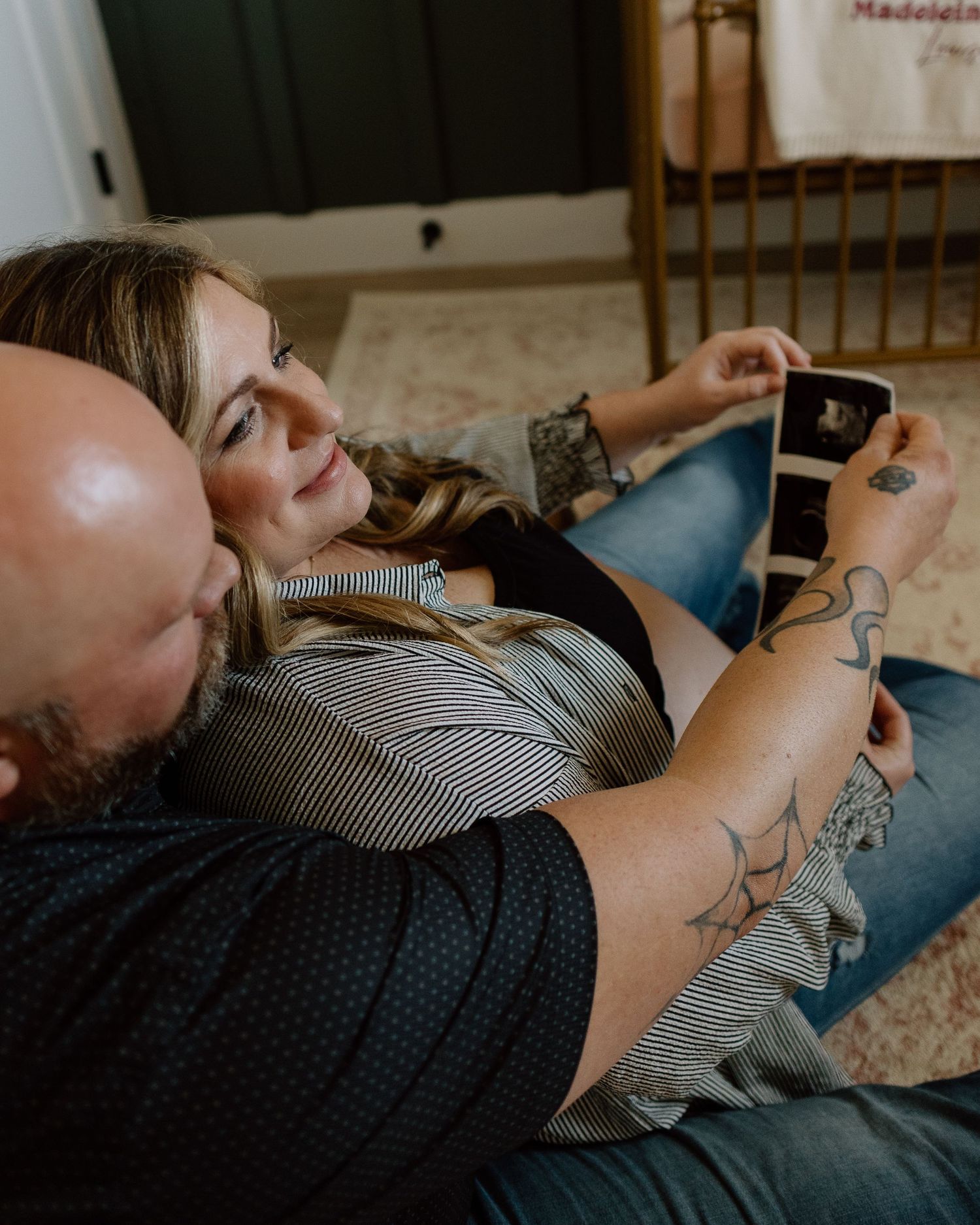 Couple relaxing on couch looking at ultrasound photos during maternity session.