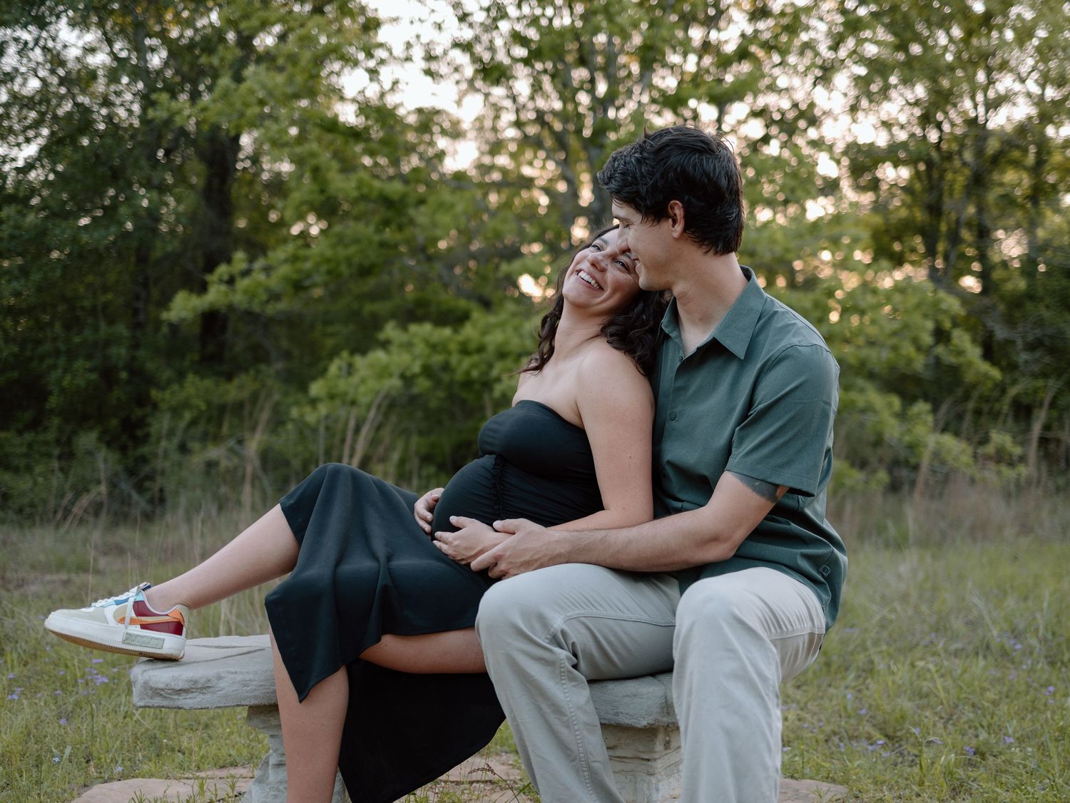 A couple relaxes together on a blanket in a field during sunset, sharing an intimate moment.