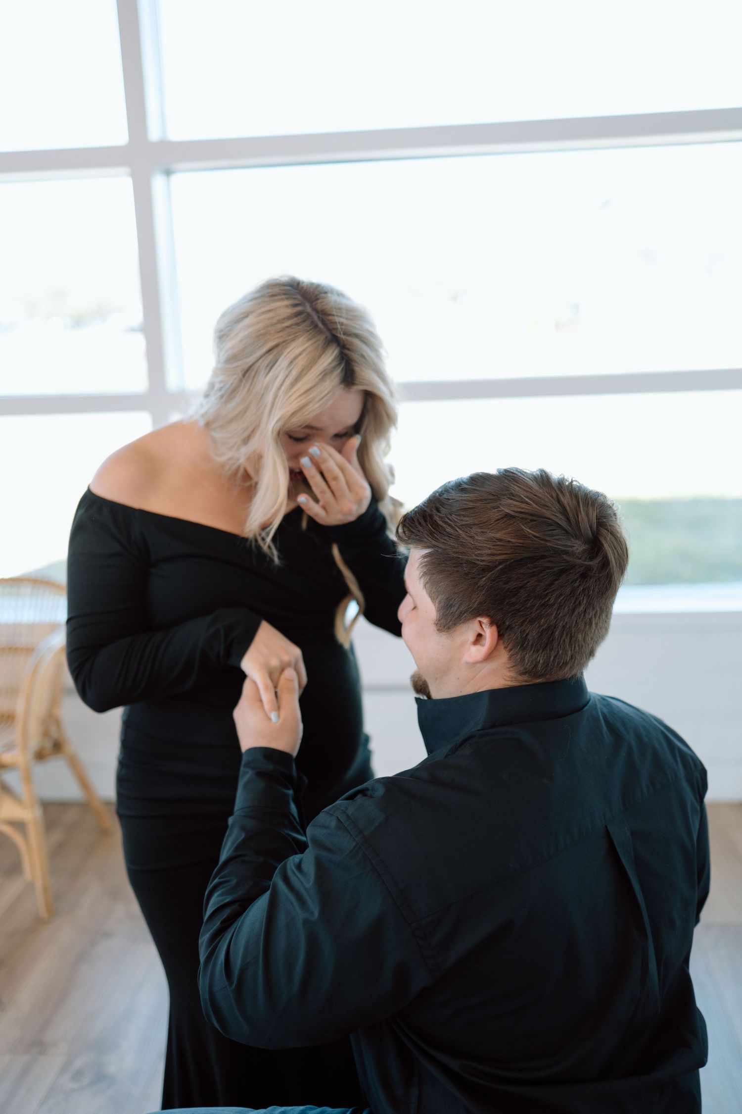 A romantic proposal moment captured by a window with natural light streaming in as someone kneels on hardwood floors.