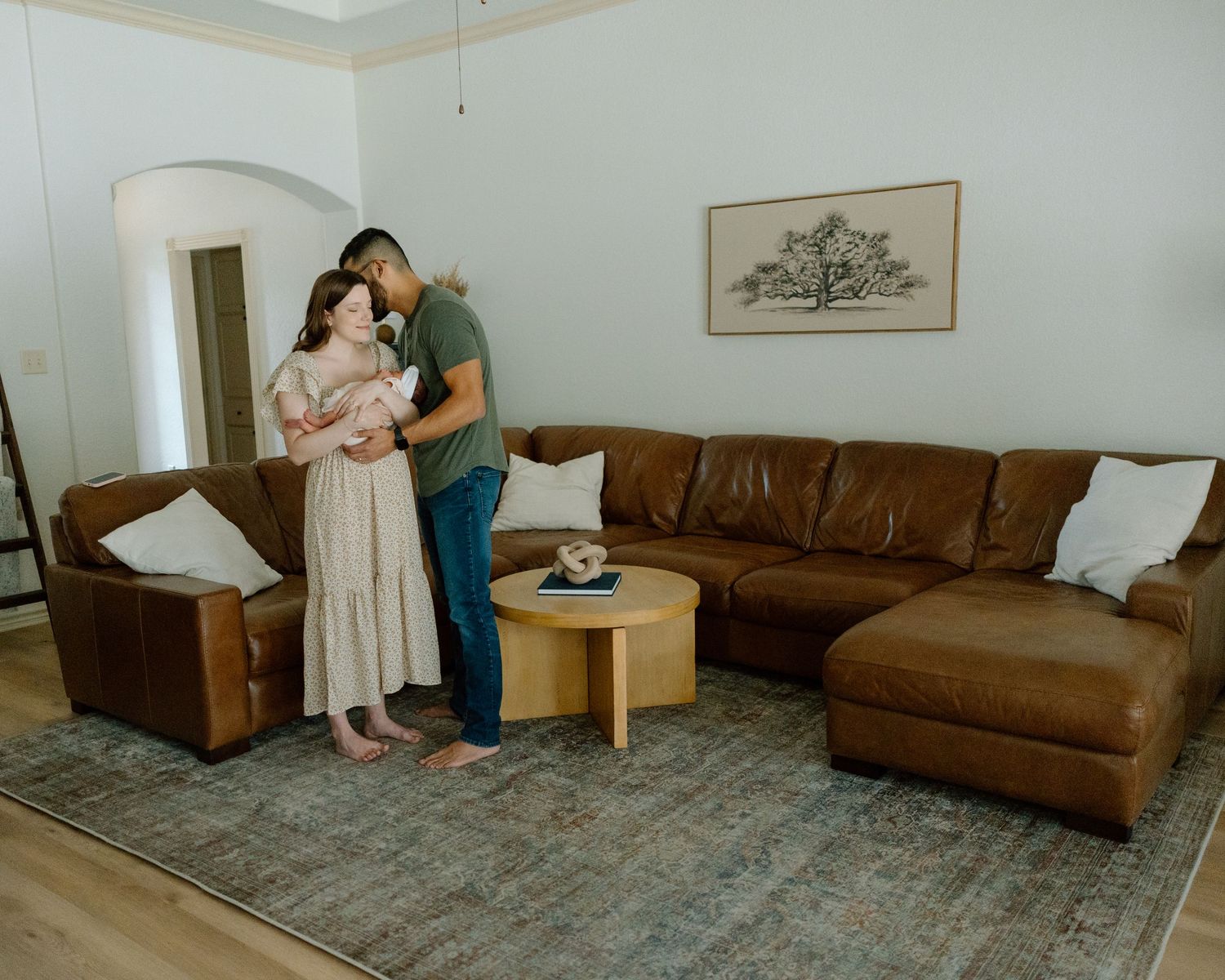 A tender family scene in a living room with brown leather sectional and minimalist wall art.
