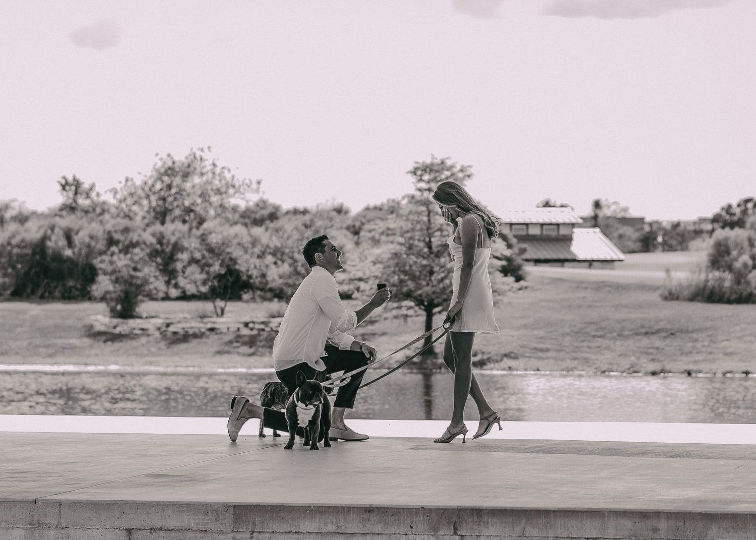 A proposal moment captured in black and white on a concrete path by the water.