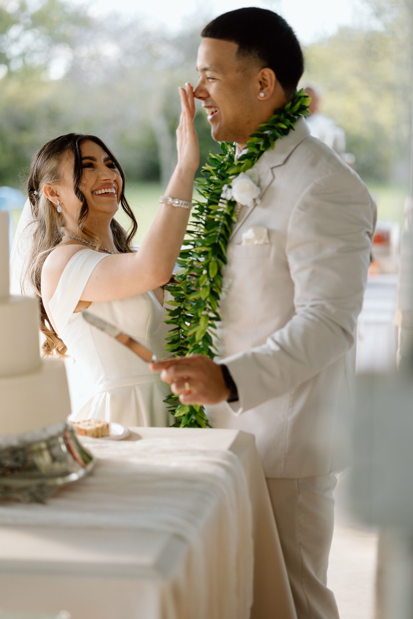 Joyful newlyweds share a playful moment during cake cutting at their Hawaiian-themed wedding reception.