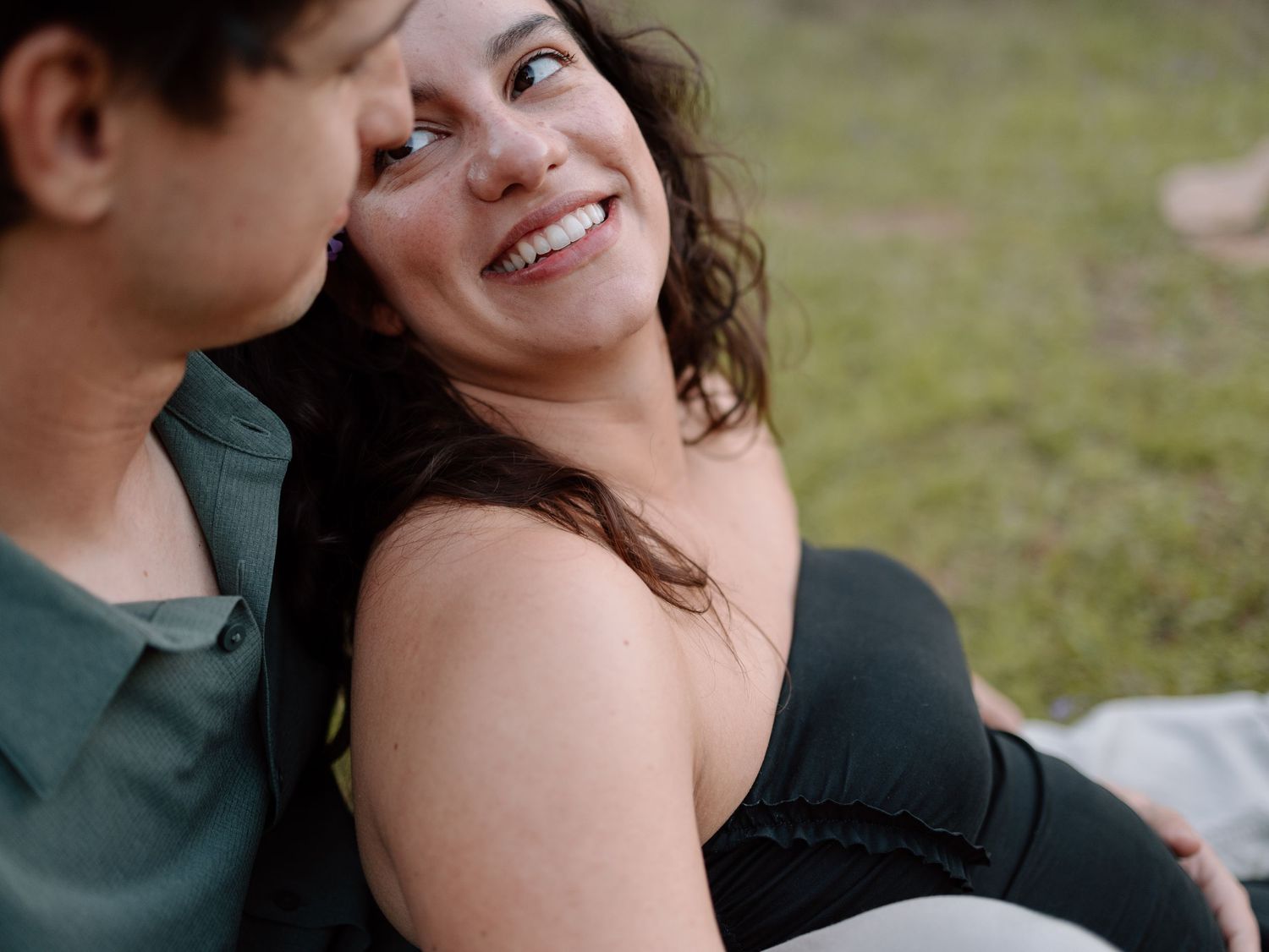 An intimate outdoor portrait of a couple sharing a tender moment on grass.