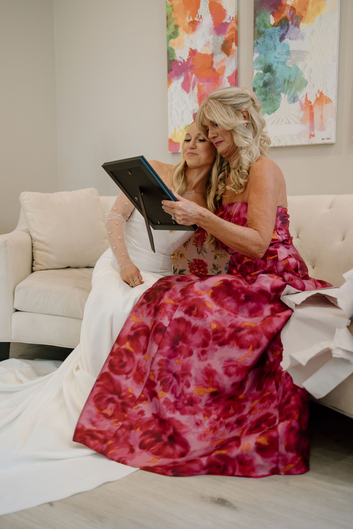 Two people in formal attire looking at tablet while seated on white couch.