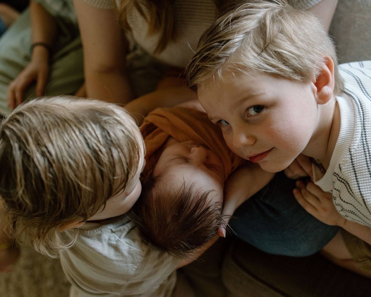 Three children lay close together while resting on a soft surface in warm natural lighting.