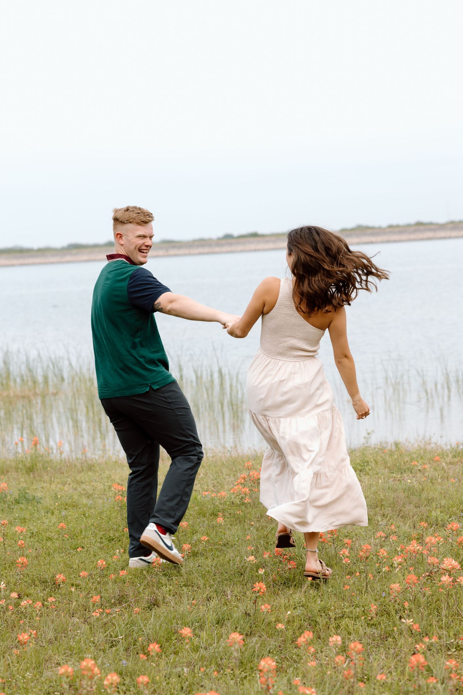 A couple dances playfully in a field of flowers near a lake.