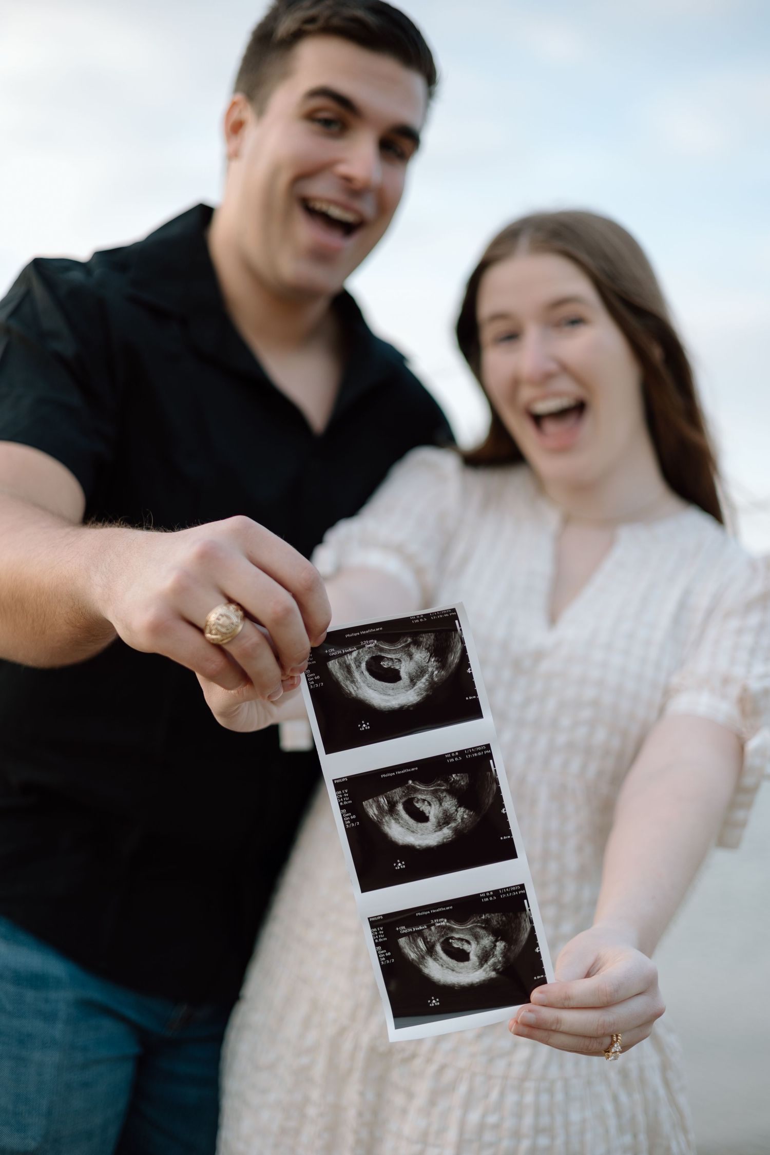 A happy couple displays ultrasound photos outdoors while sharing their pregnancy announcement.
