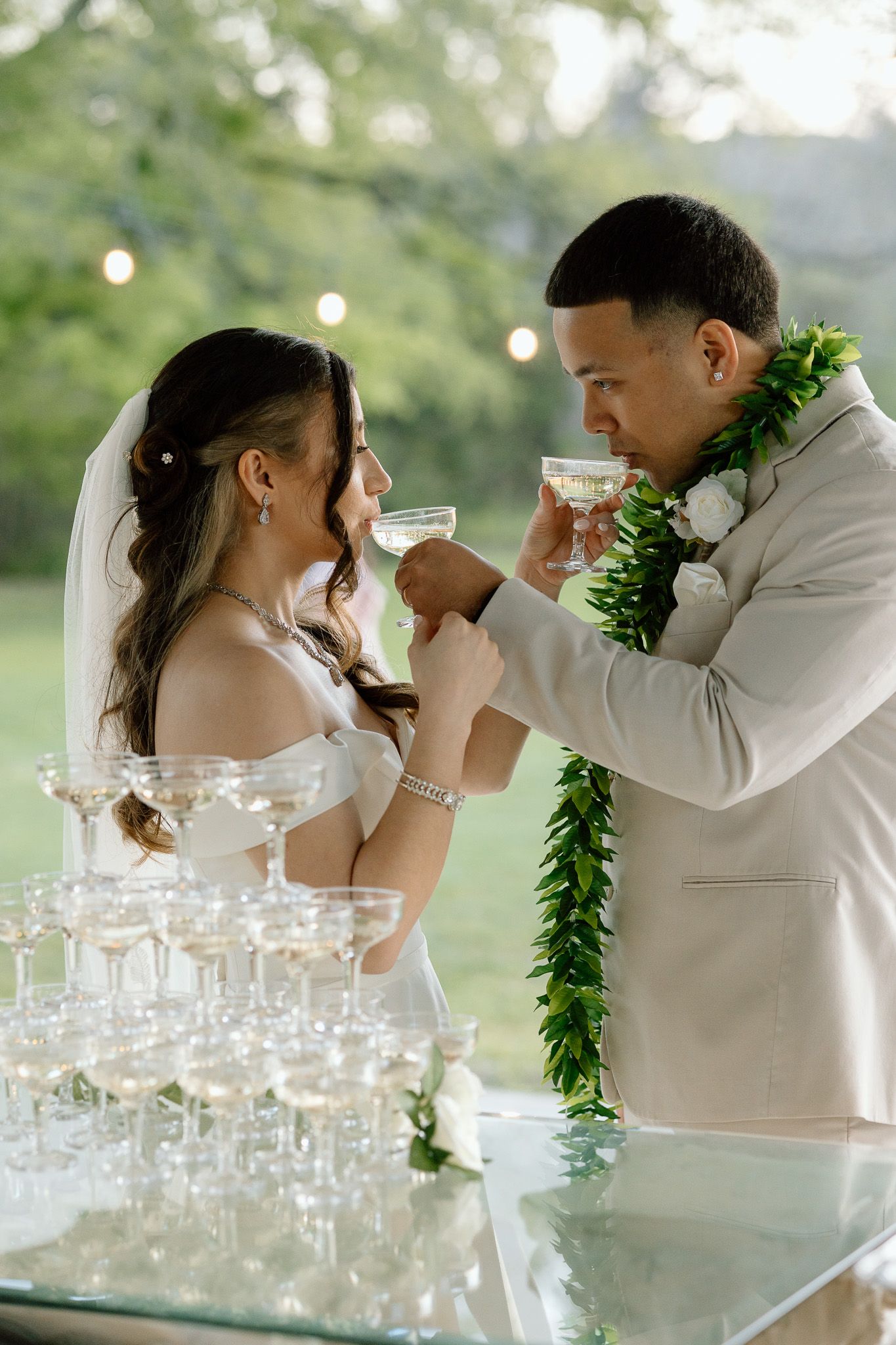 Newlyweds share champagne toast at outdoor wedding reception with glass tower display.