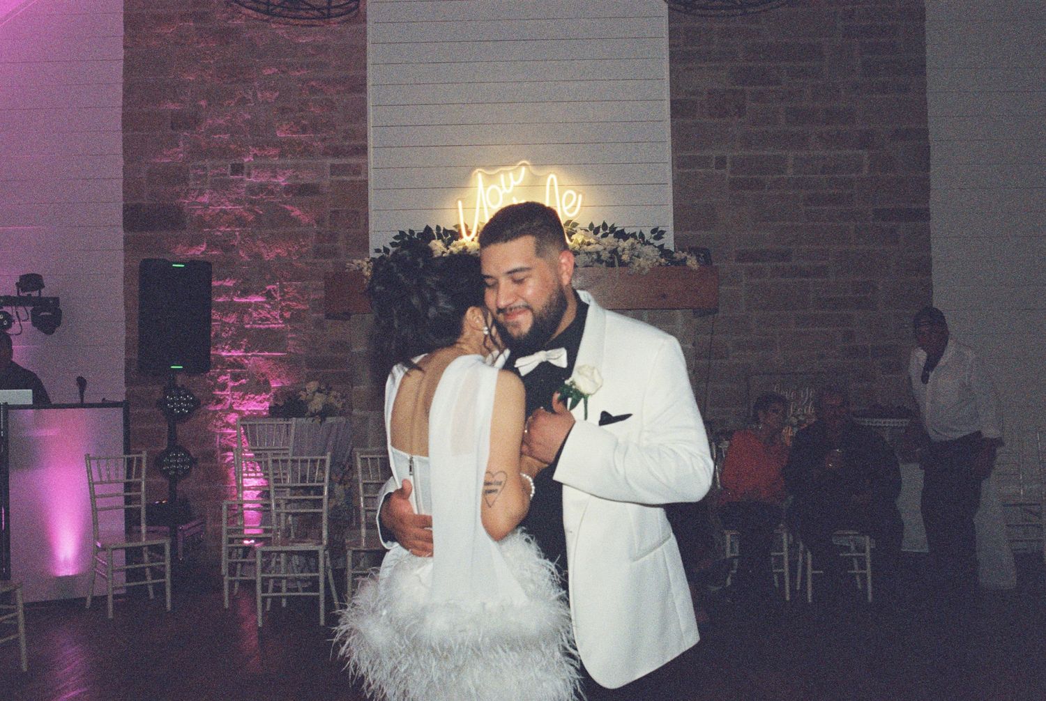 Couple sharing an intimate slow dance moment at their reception with mood lighting and brick walls.