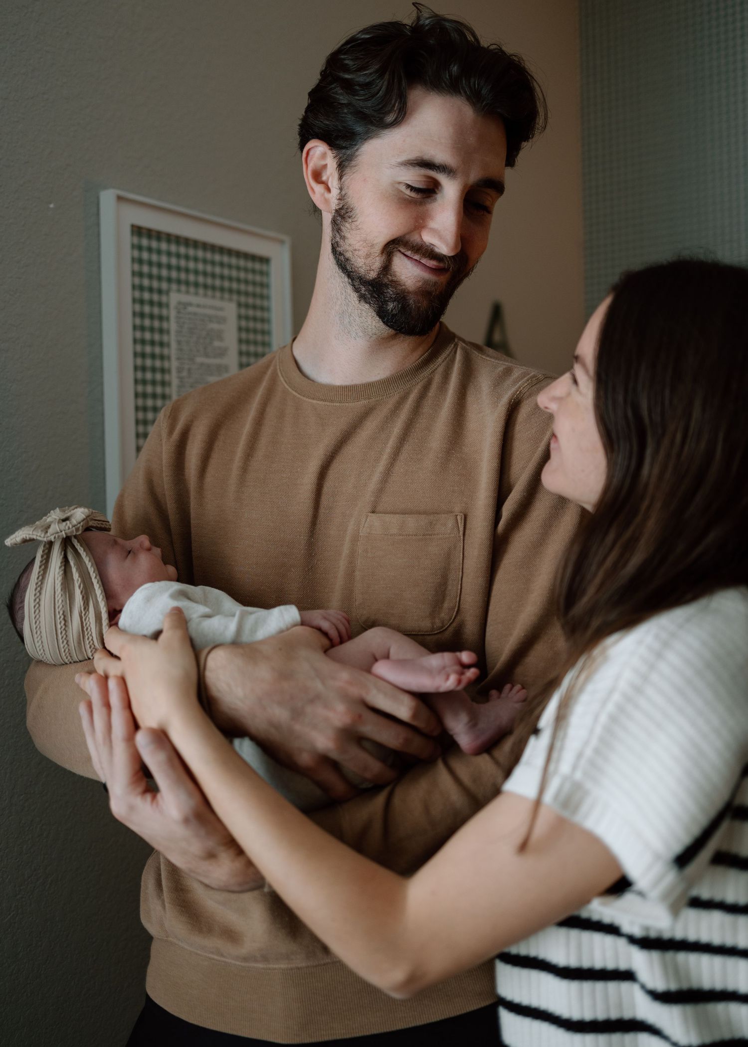 New parents gazing lovingly at each other while holding their swaddled infant.