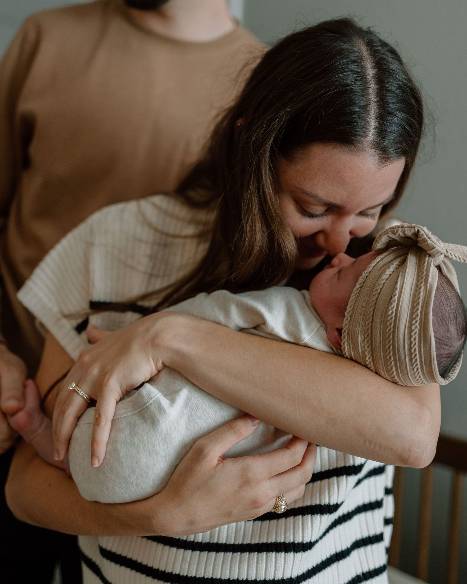 A tender moment between parent and newborn baby swaddled in light colored fabric.