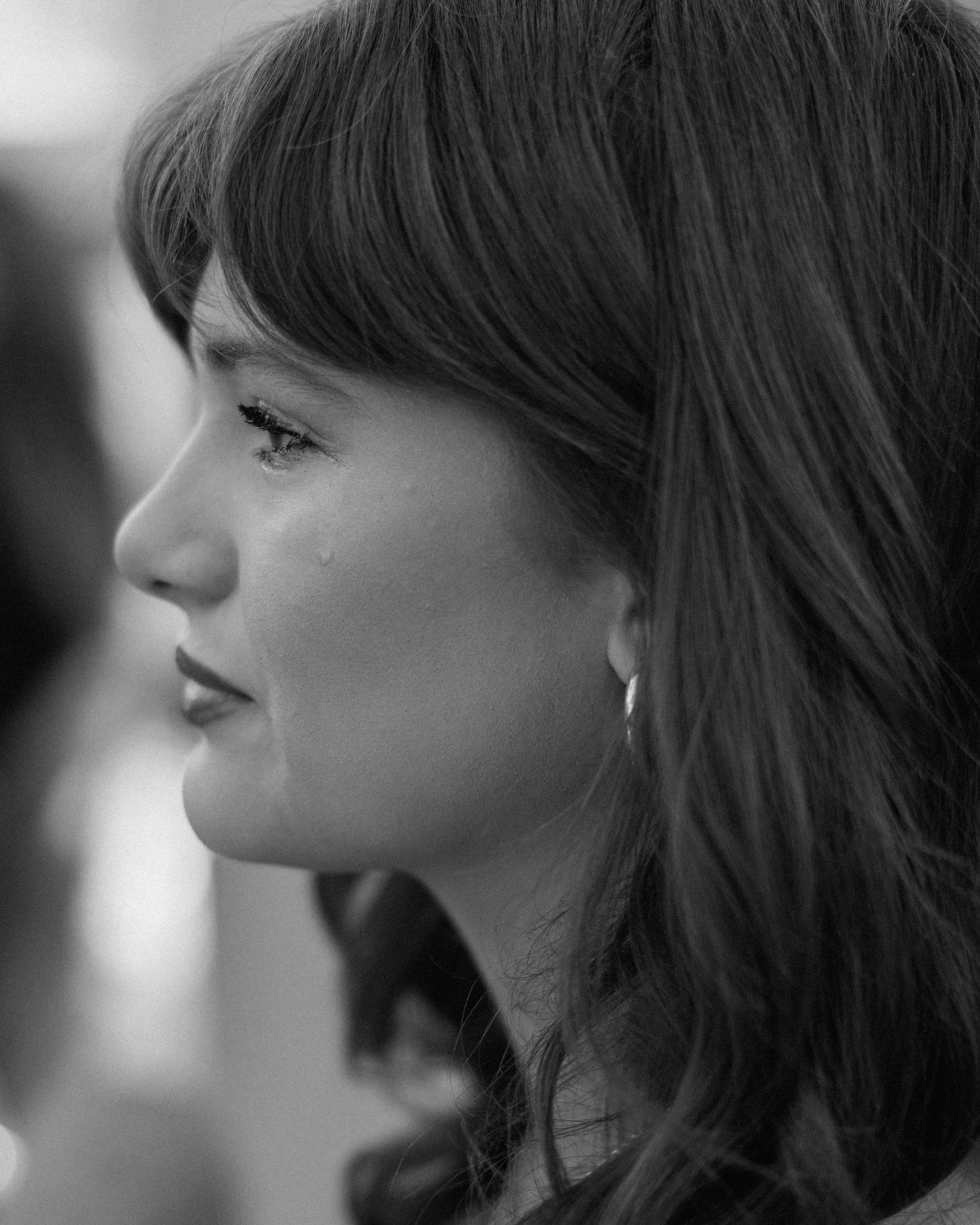 Black and white profile portrait of a young woman with bangs and hoop earring, looking thoughtful.