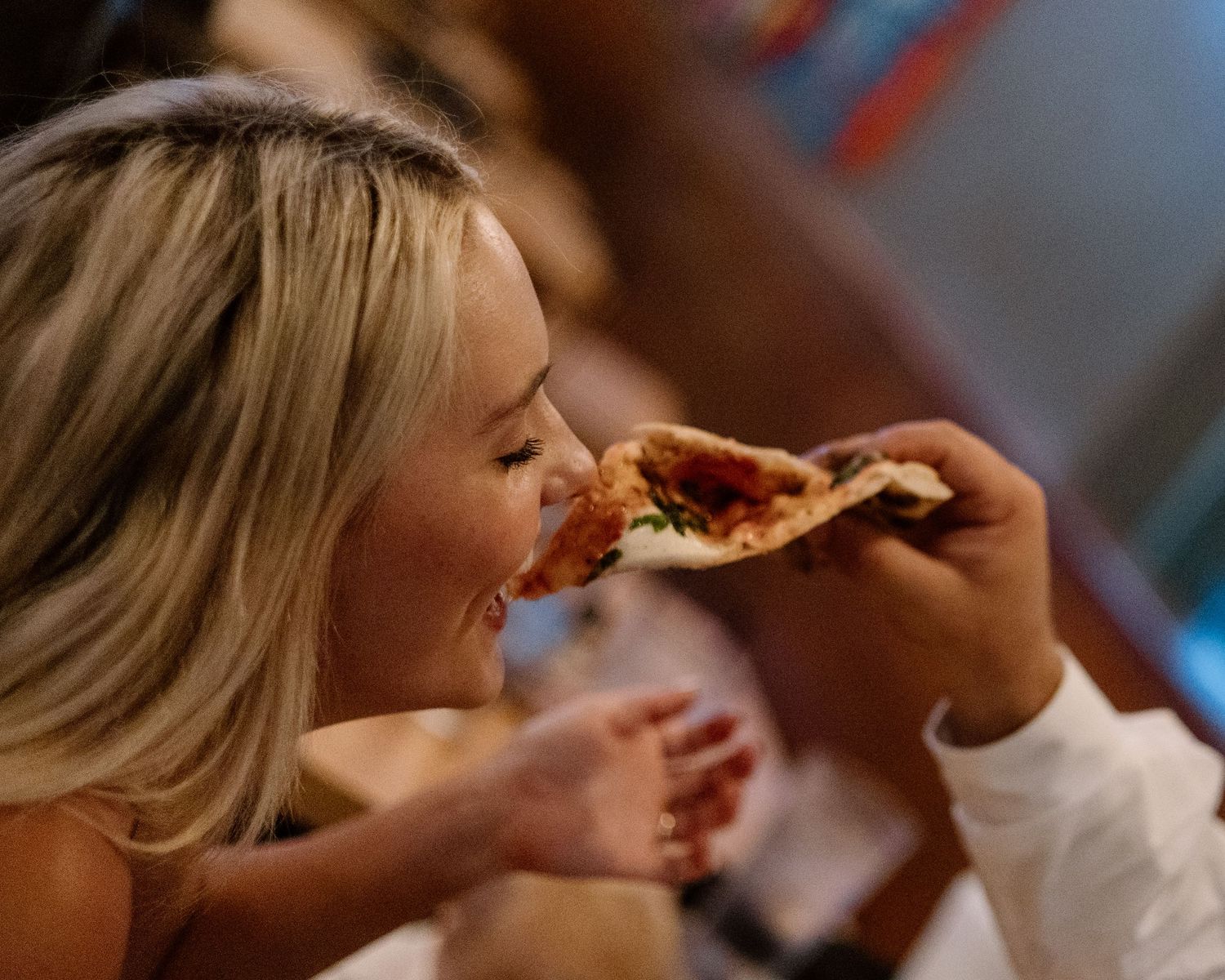 Woman taking a bite of a delicious pizza slice at a restaurant, enjoying a cheesy Italian meal.