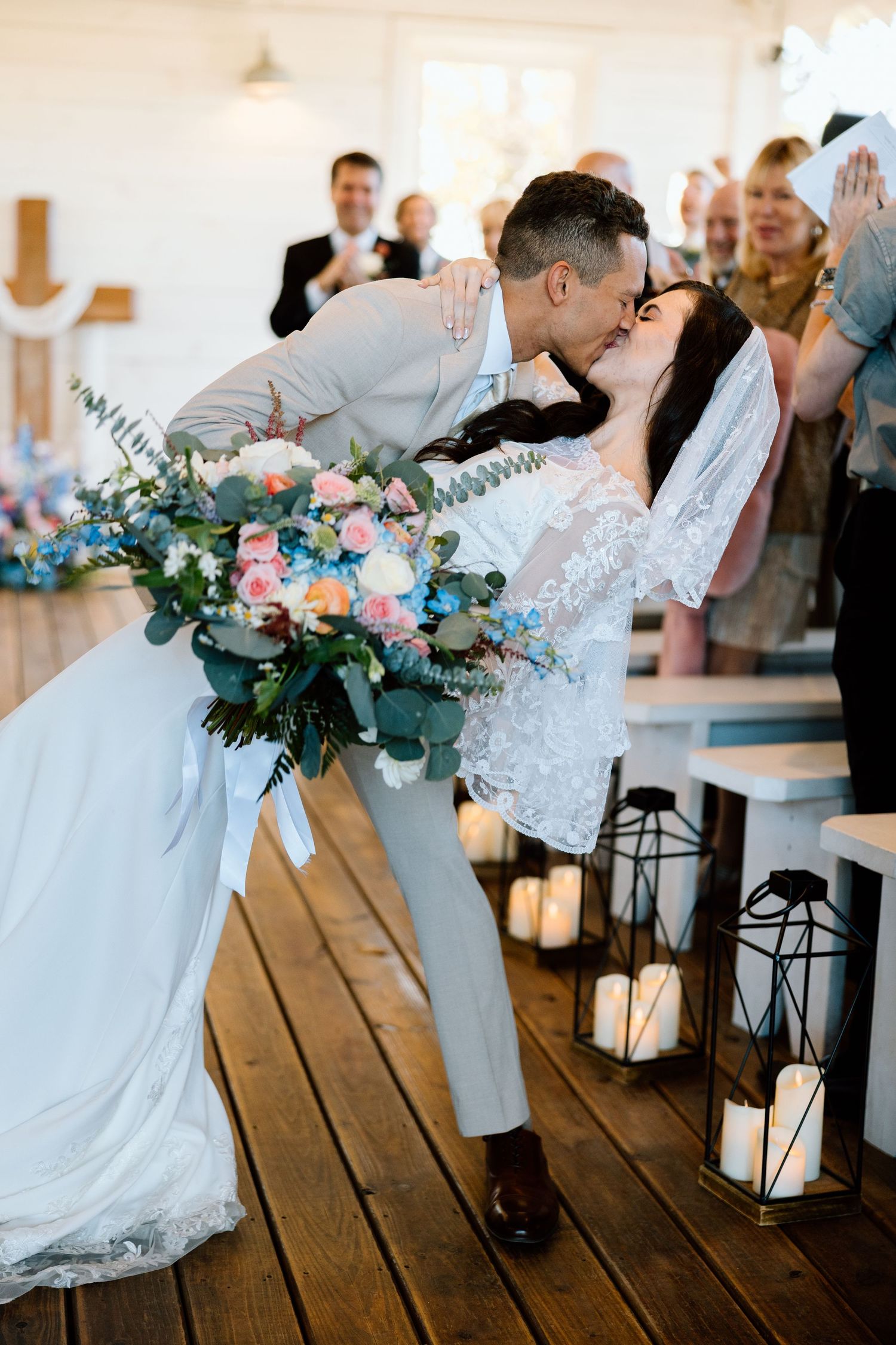 Groom dipping bride for kiss in aisle holding colorful floral bouquet.