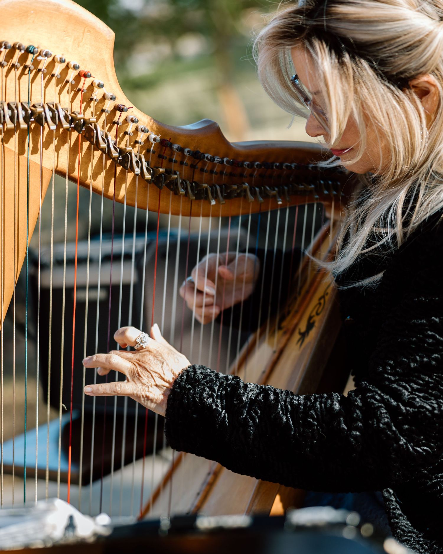 Blonde woman playing a wooden harp outdoors at a wedding ceremony.