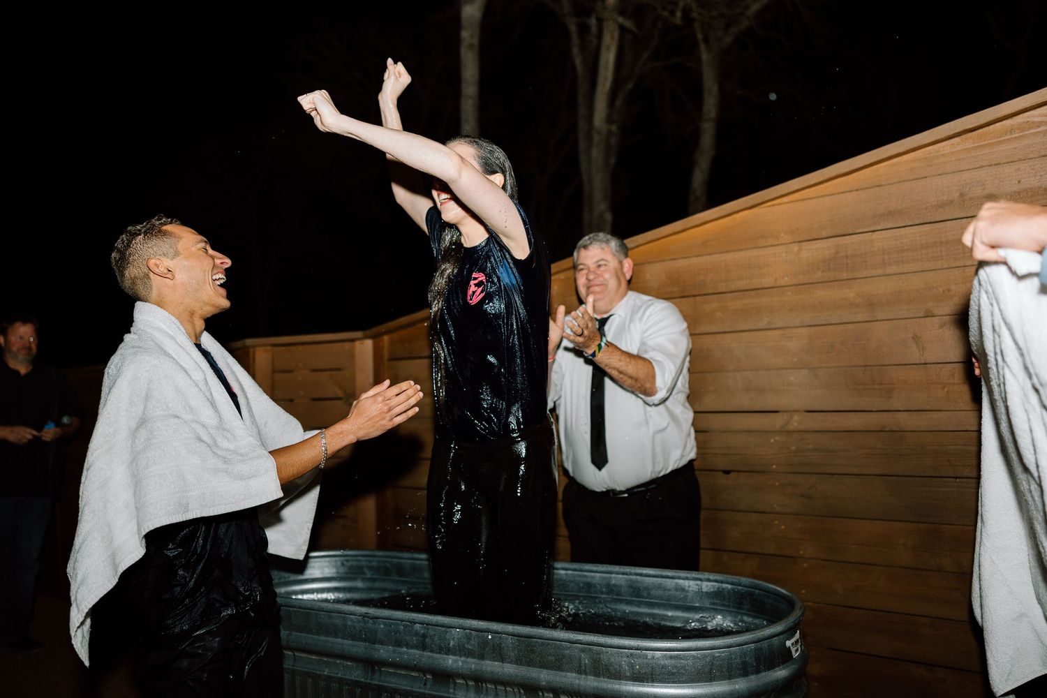 Joyful person standing in galvanized tub at night outdoor celebration with cheering guests.