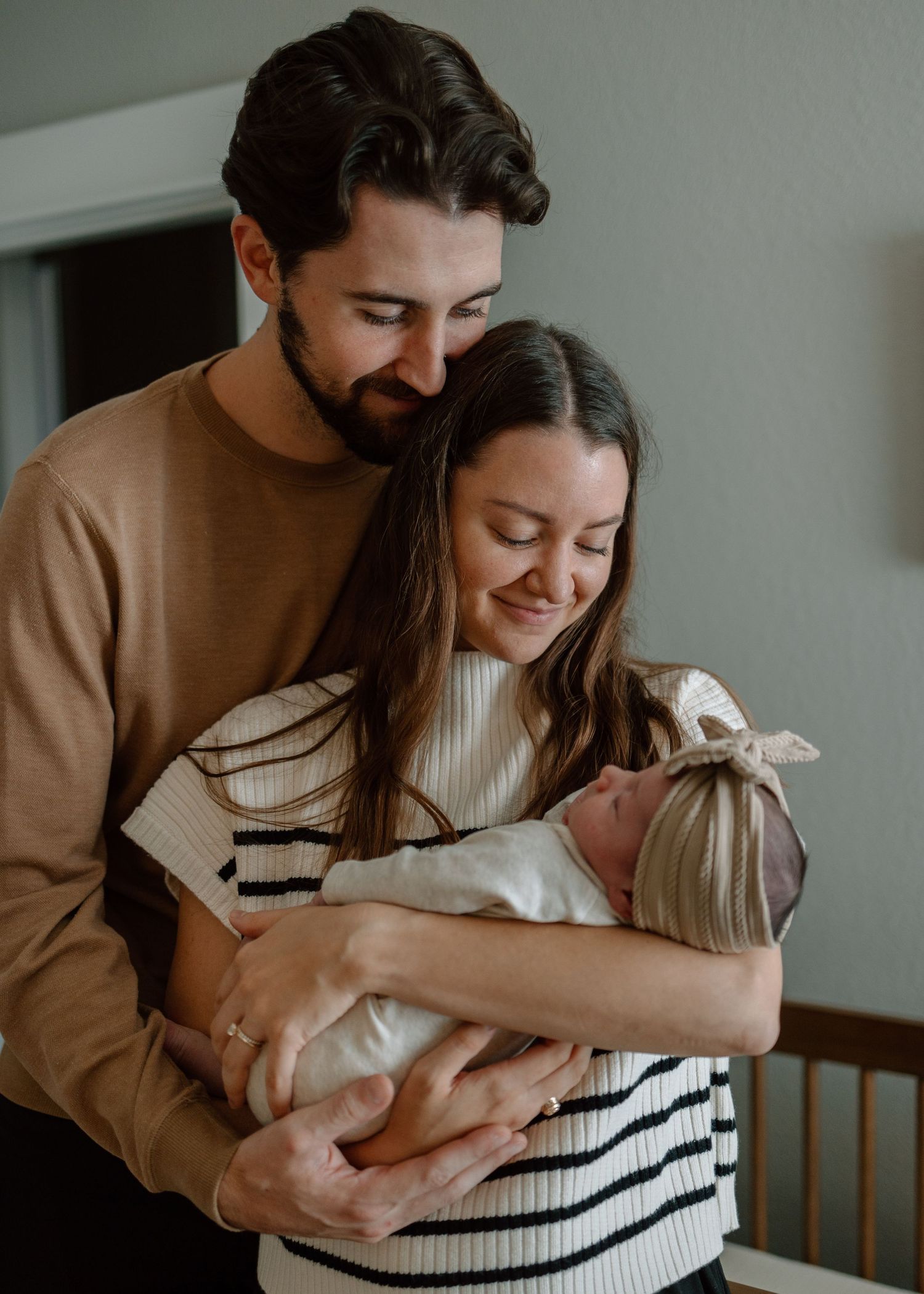 Tender family moment with baby in nursery setting and soft natural light.