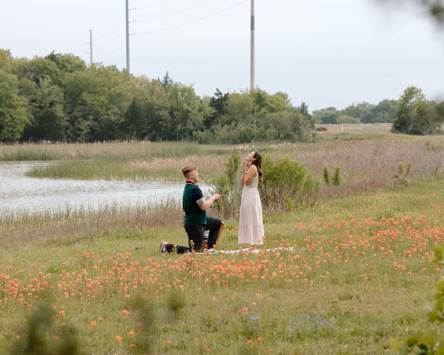 A proposal moment captured in a field of orange wildflowers beside a lake.