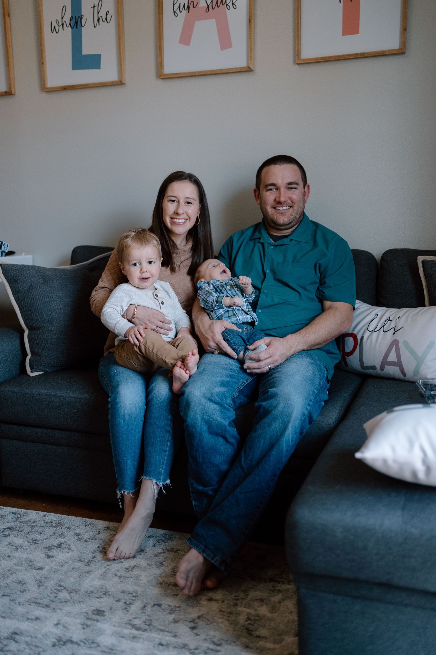 Young family relaxing together on a gray sectional couch in a modern living room with decorative wall art.