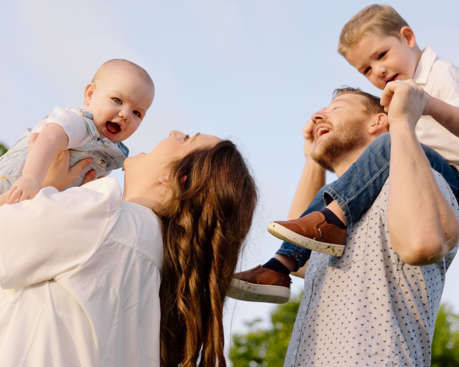 Joyful family laughing and playing together outdoors during golden hour in the summer.