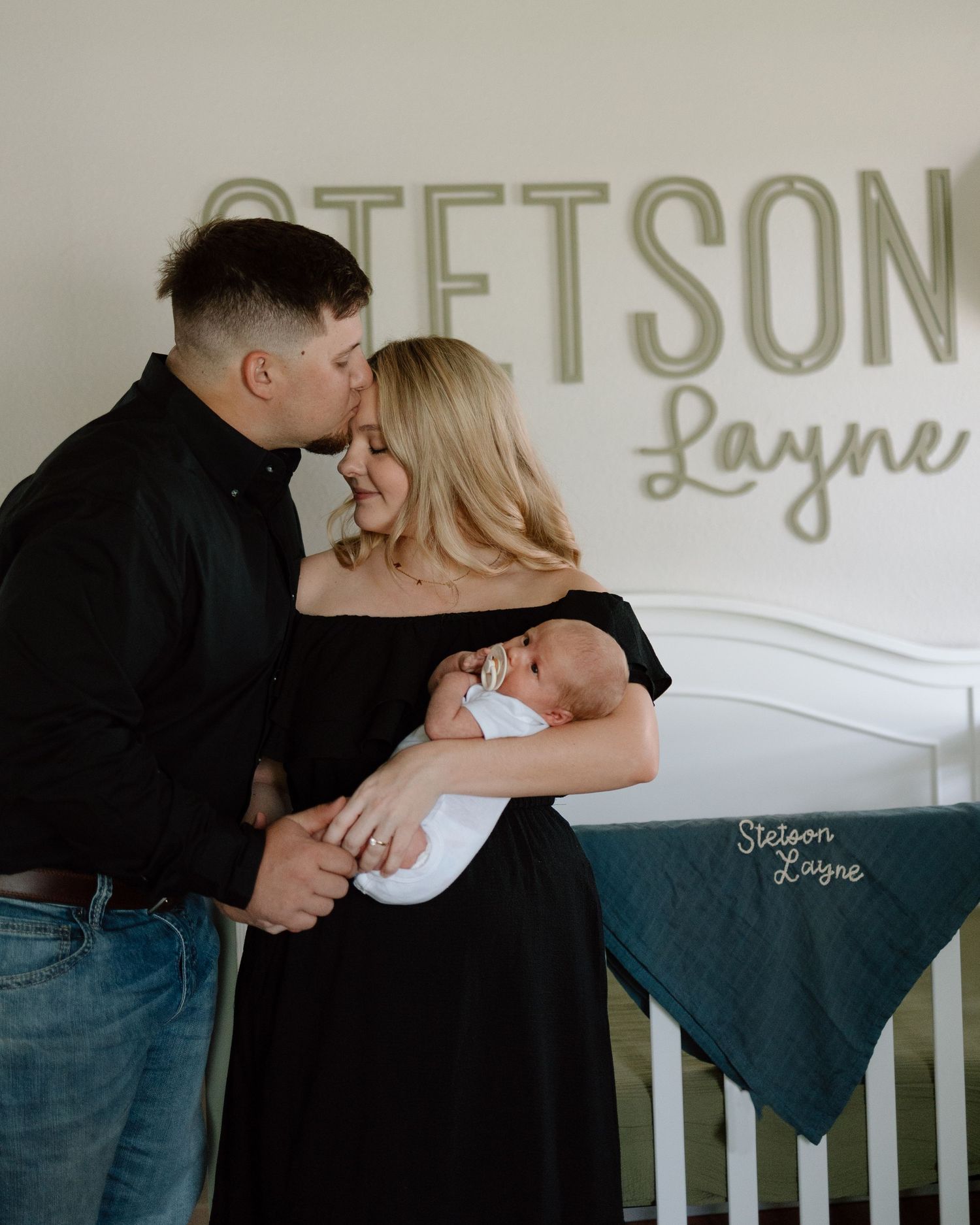 Parents share intimate moment with newborn baby in front of wall with name Stetson Layne displayed.