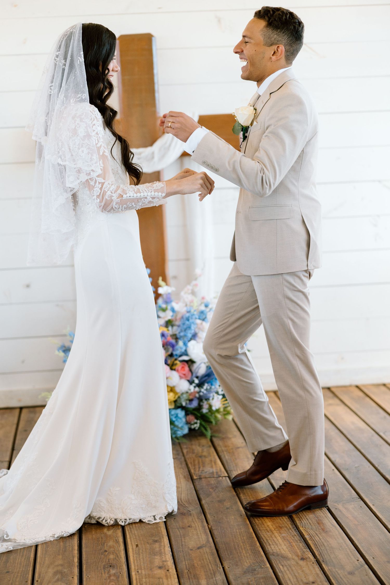 Bride and groom sharing first dance in rustic white barn with floral arrangements.
