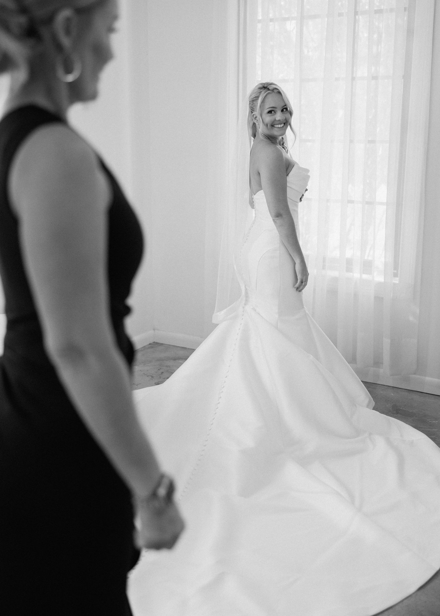 Black and white photo of bride in mermaid wedding gown with long train smiling over her shoulder.