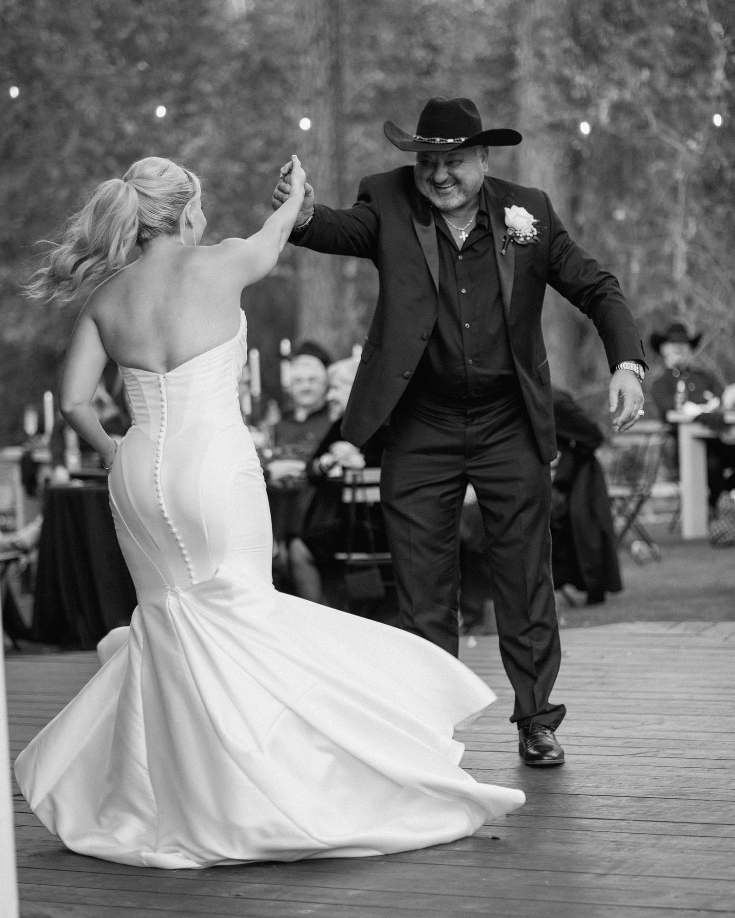 Black and white photo of bride dancing with man in black cowboy hat and suit at wedding reception.