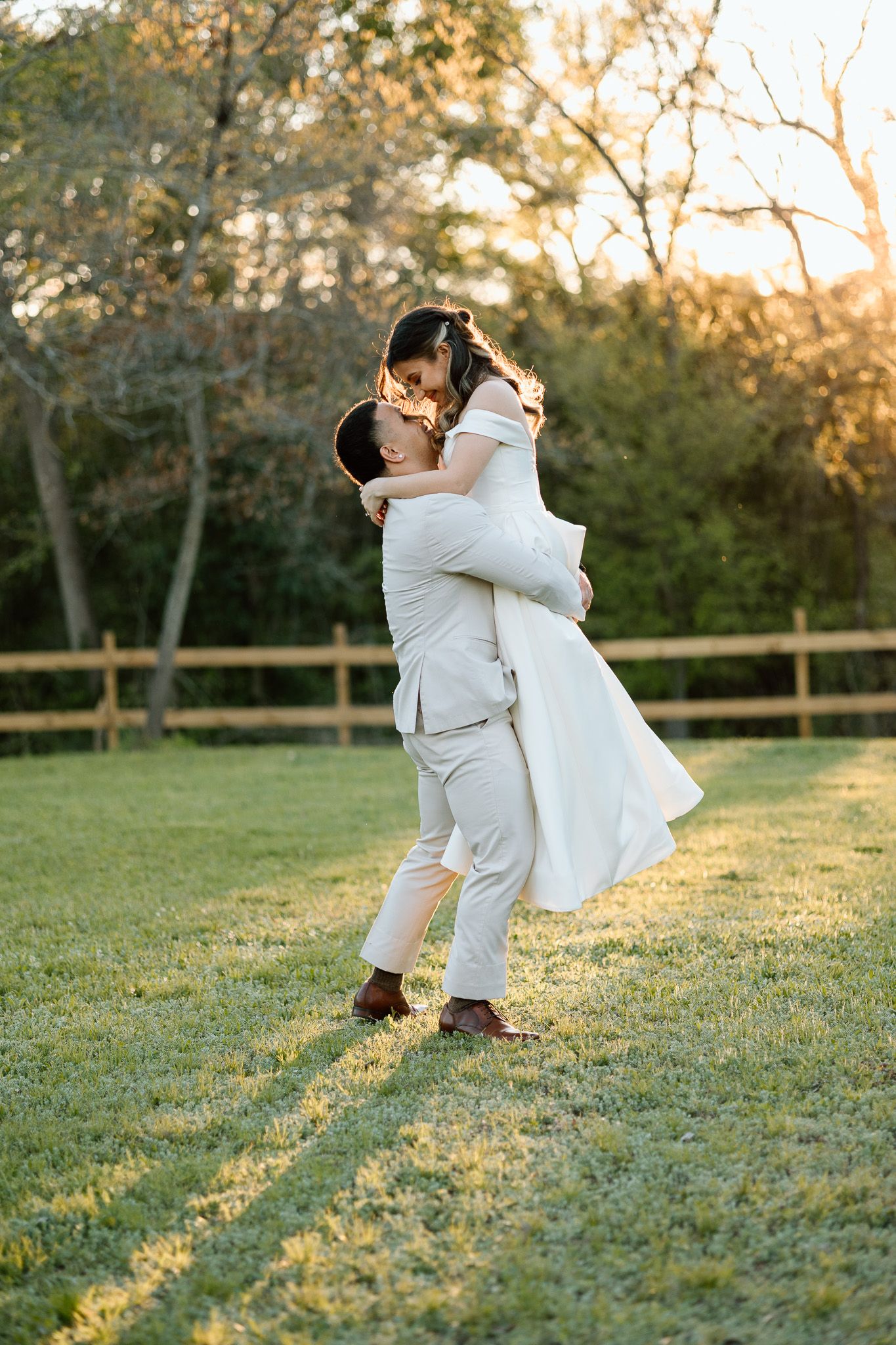Groom lifts bride in a joyful embrace during sunset on their wedding day.