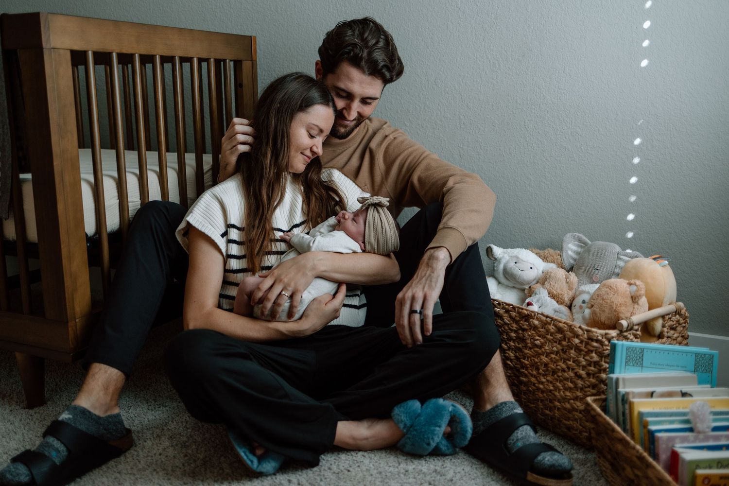 Parents sitting on floor near wooden crib sharing moment with newborn.