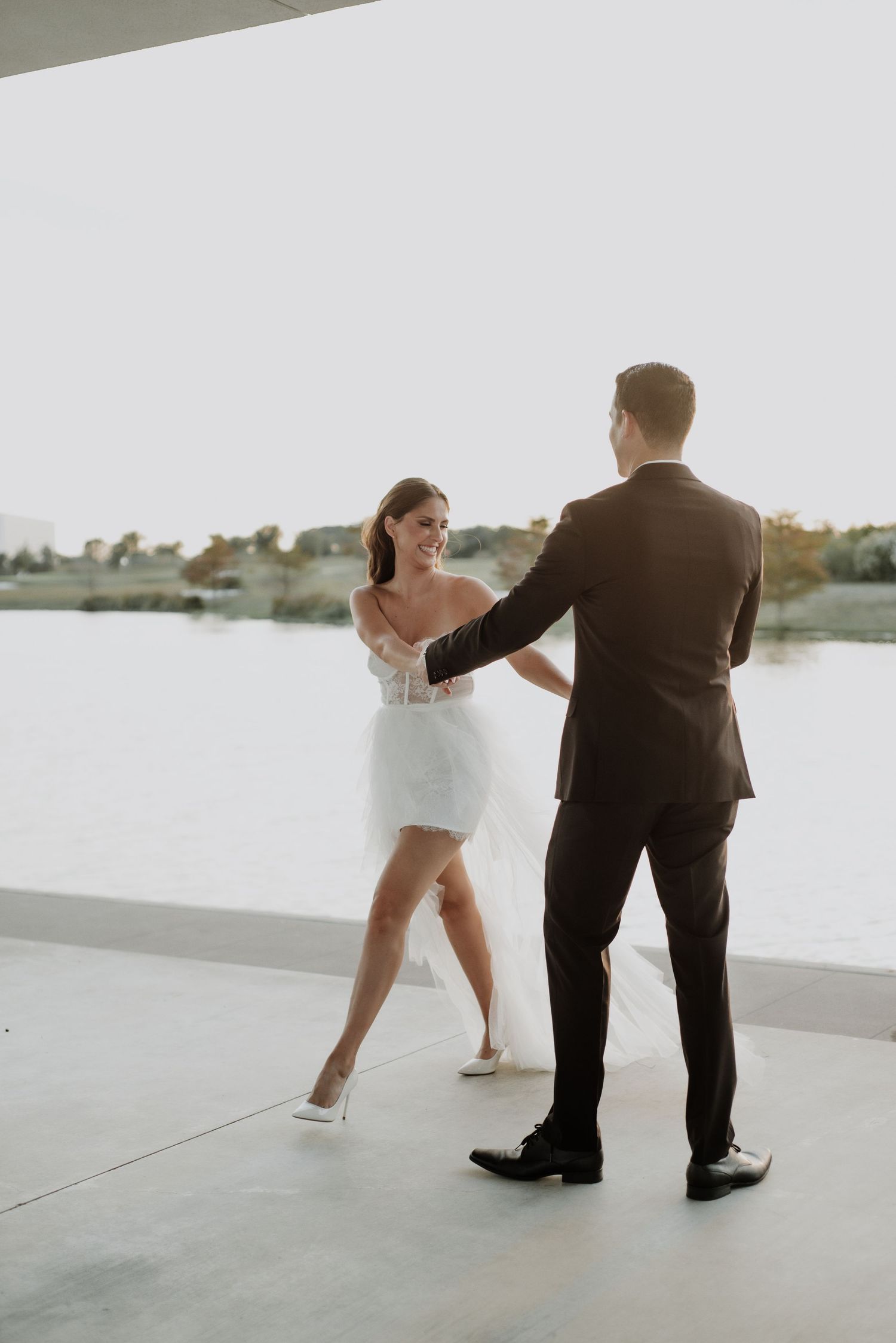 A couple in formal attire shares a dance moment on a bright modern patio overlooking water.
