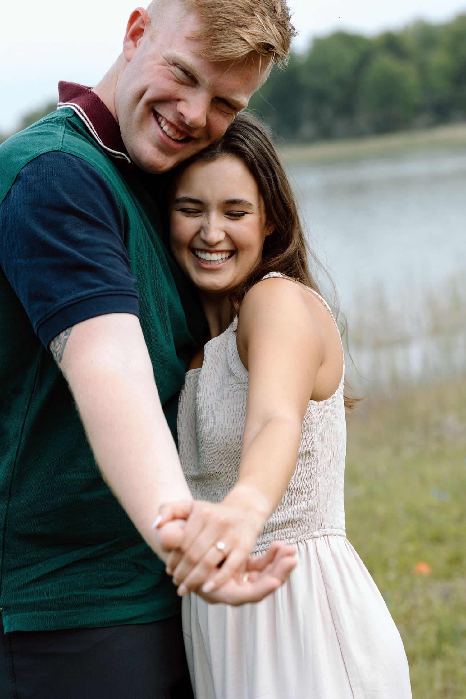 A joyful couple laughs together while embracing in a casual outdoor setting by a lake.