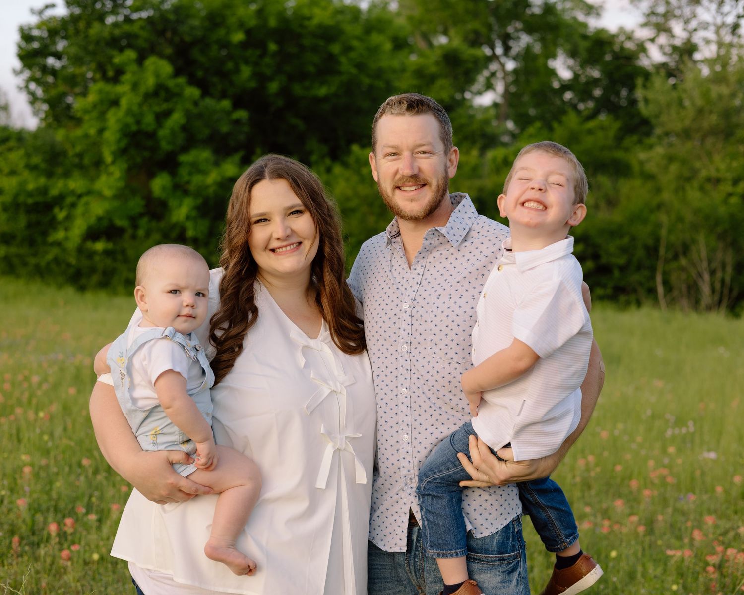 A smiling family poses together in a green meadow during golden hour.