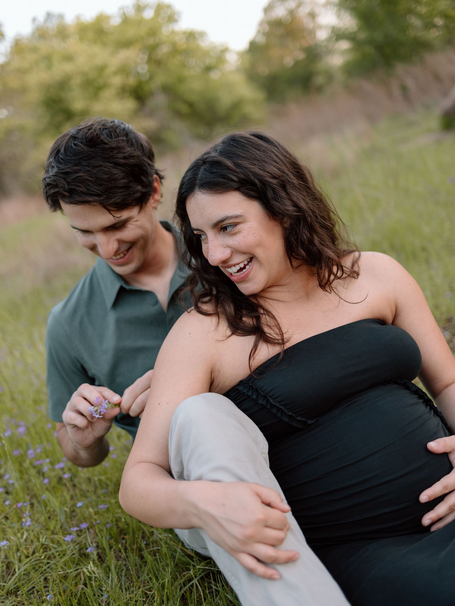 A couple shares laughter while sitting together in a sunlit field.