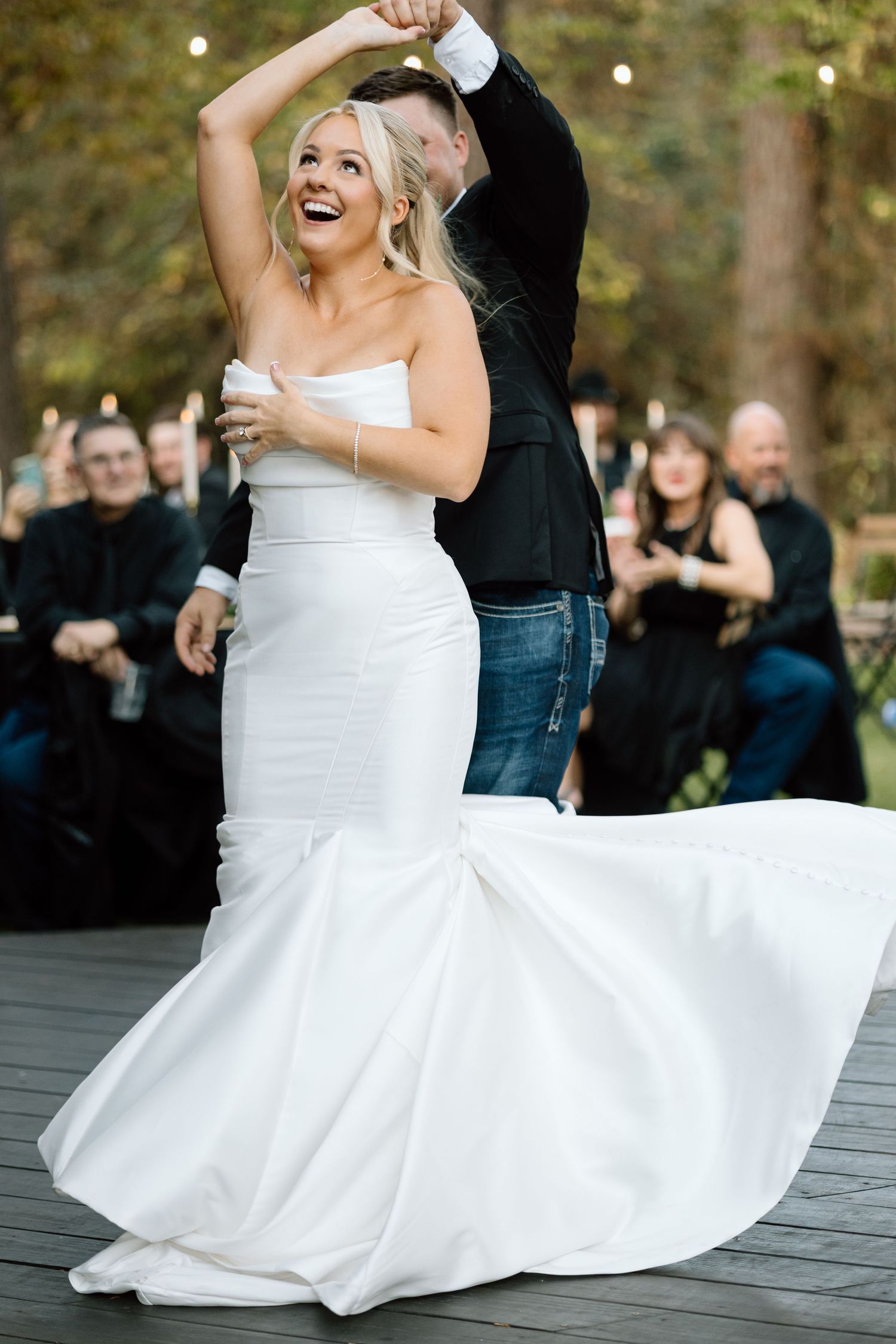Bride in white strapless mermaid gown twirls joyfully with groom during outdoor wedding reception first dance.