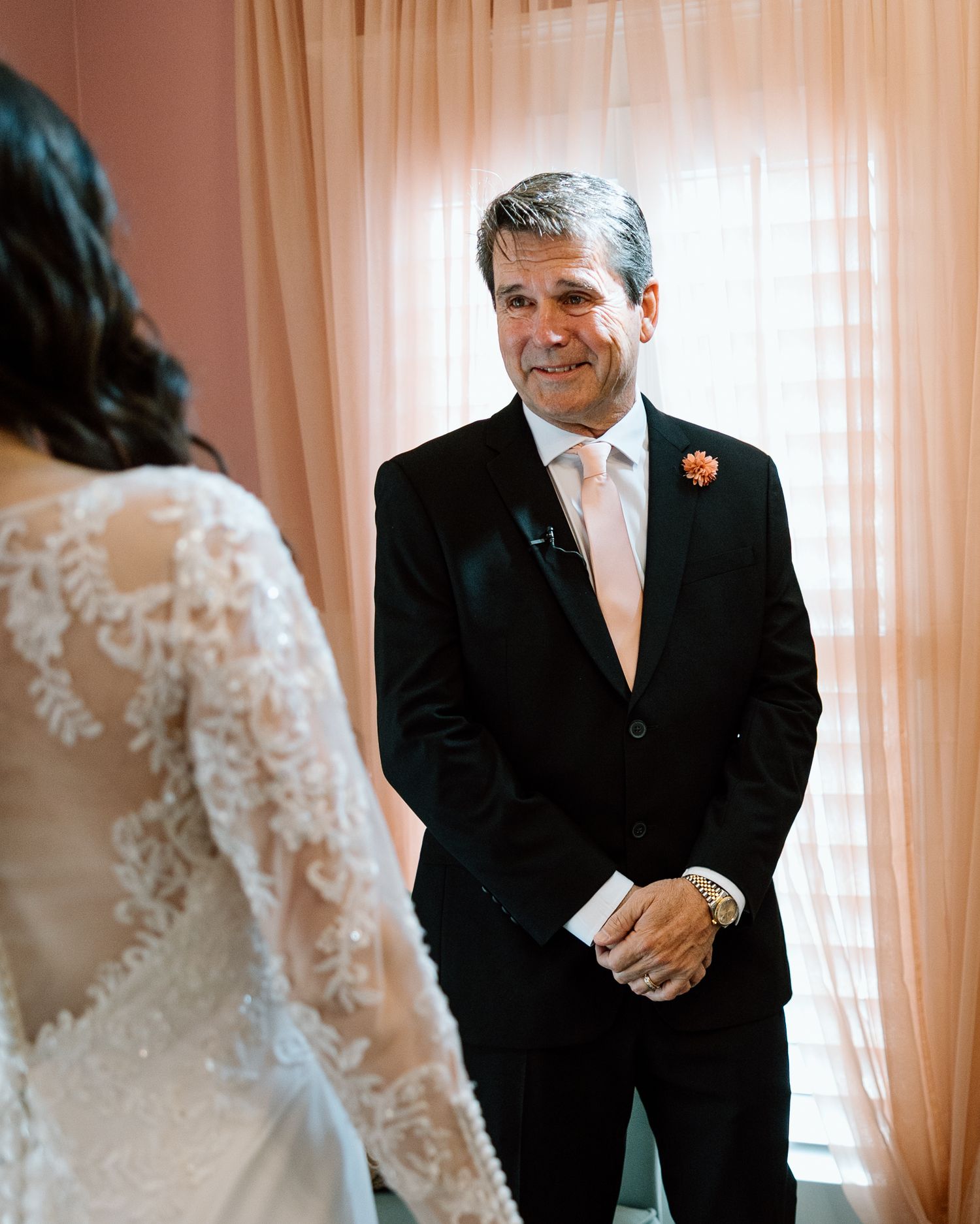 Emotional father seeing bride daughter in lace wedding gown for the first time, wearing black suit with boutonniere.