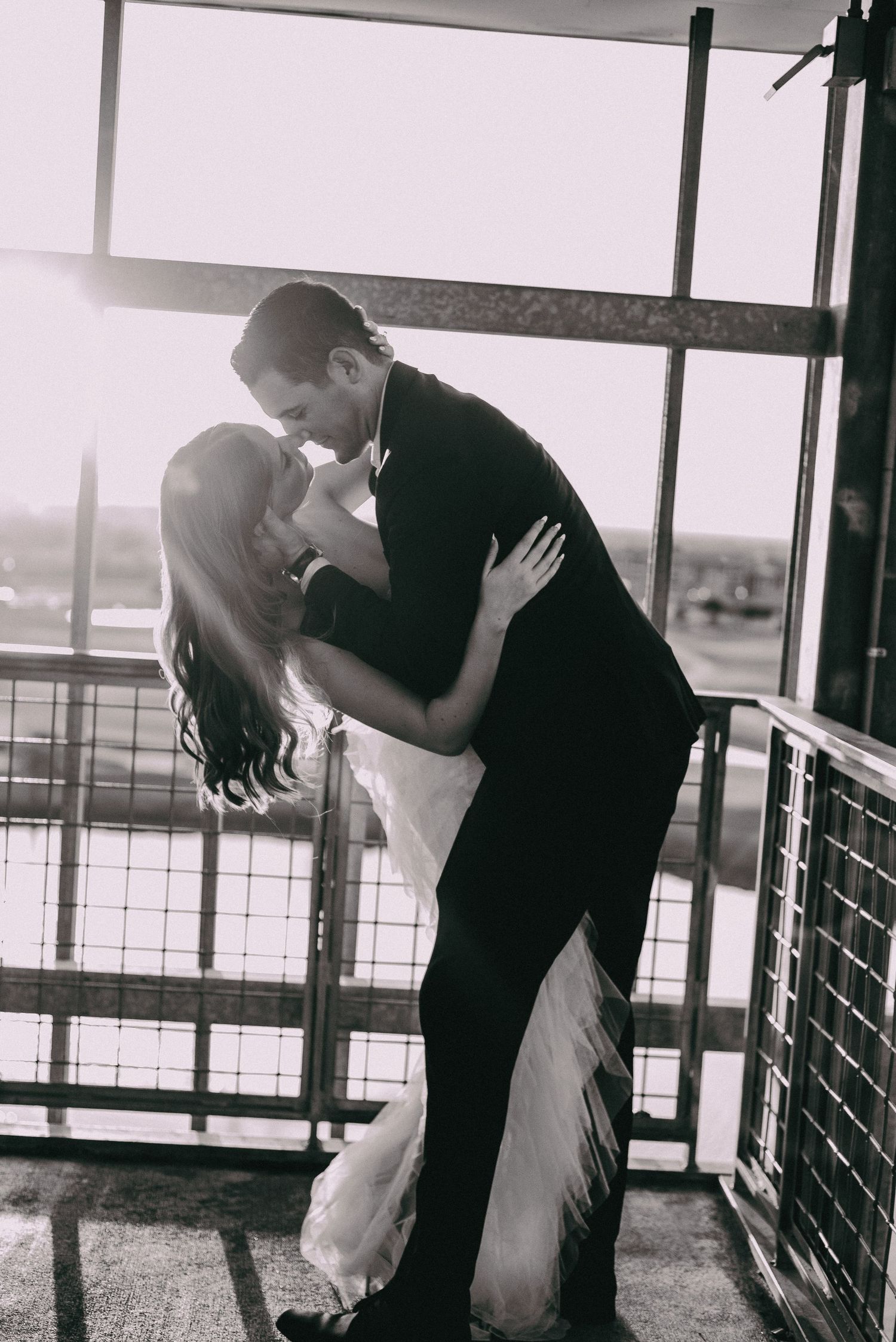 A black and white romantic dip kiss on a balcony with railing- cinematic wedding photography college station Texas