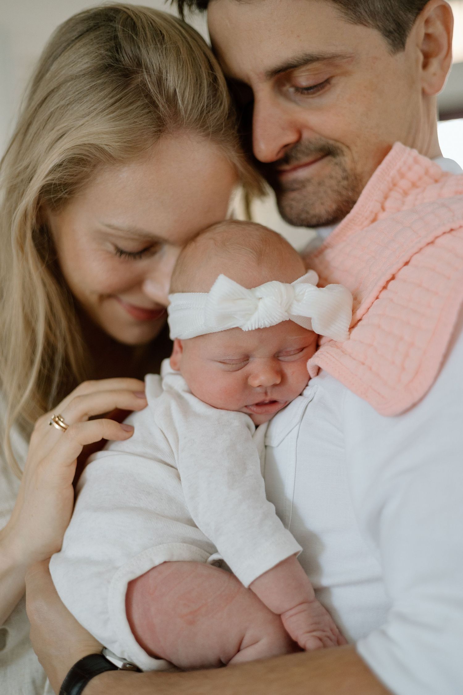 Tender family moment with parents embracing sleeping newborn in white outfit.