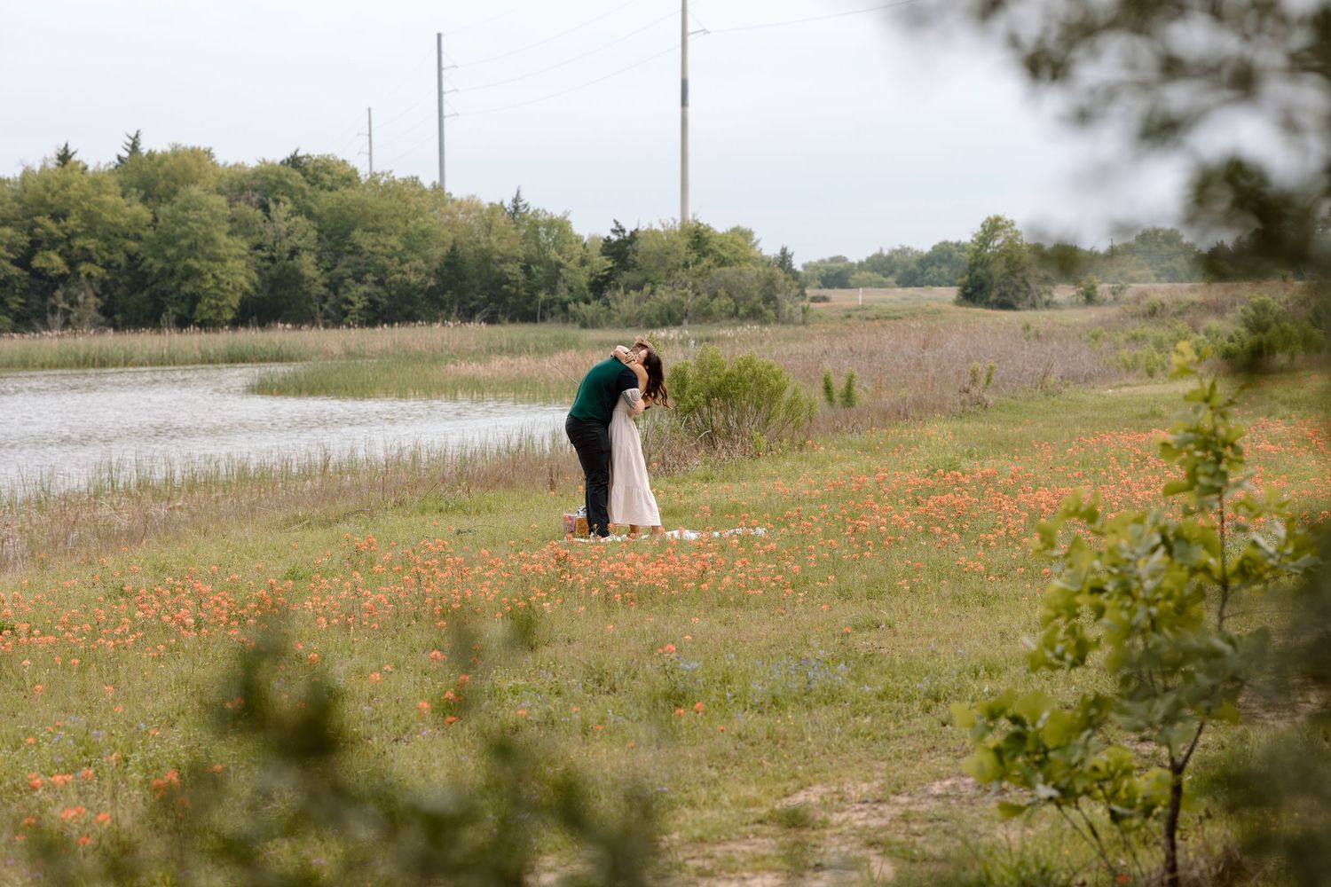 A romantic scene with two figures standing among orange wildflowers near a peaceful lake documentary photography college station Texas.