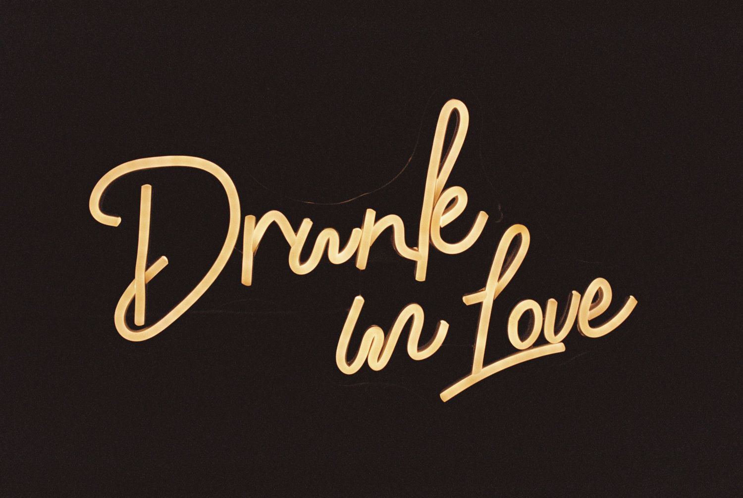 A decorative neon sign reading 'Drunk in Love' in cursive gold lettering against a dark background.