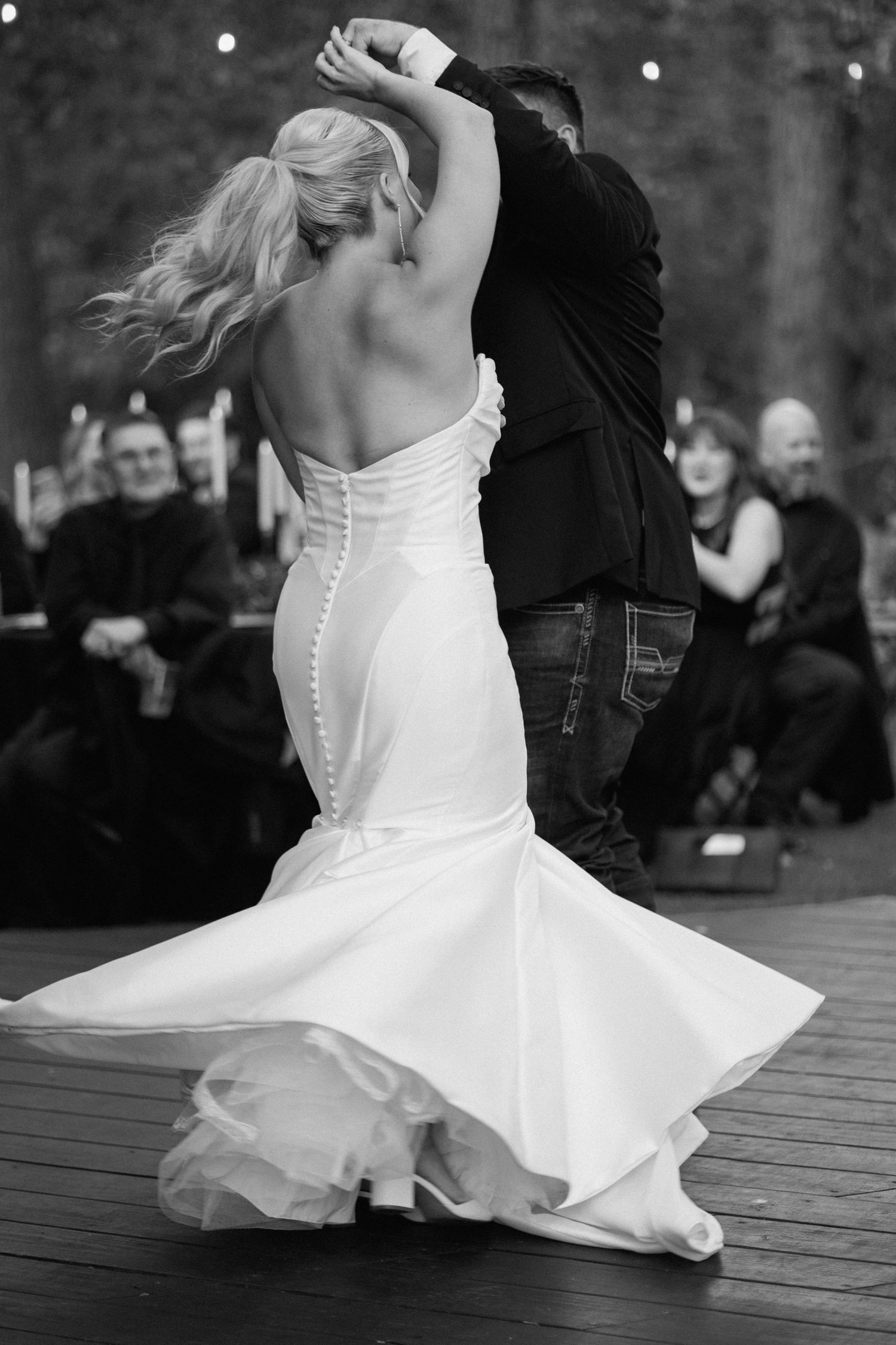 Black and white photo of bride twirling in mermaid gown during first dance at outdoor wedding reception.