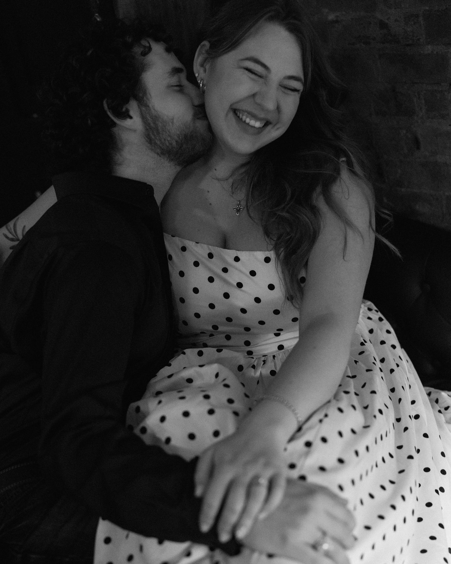 Black and white photo of a smiling couple, woman in polka dot dress, man in dark suit nuzzling her cheek.
