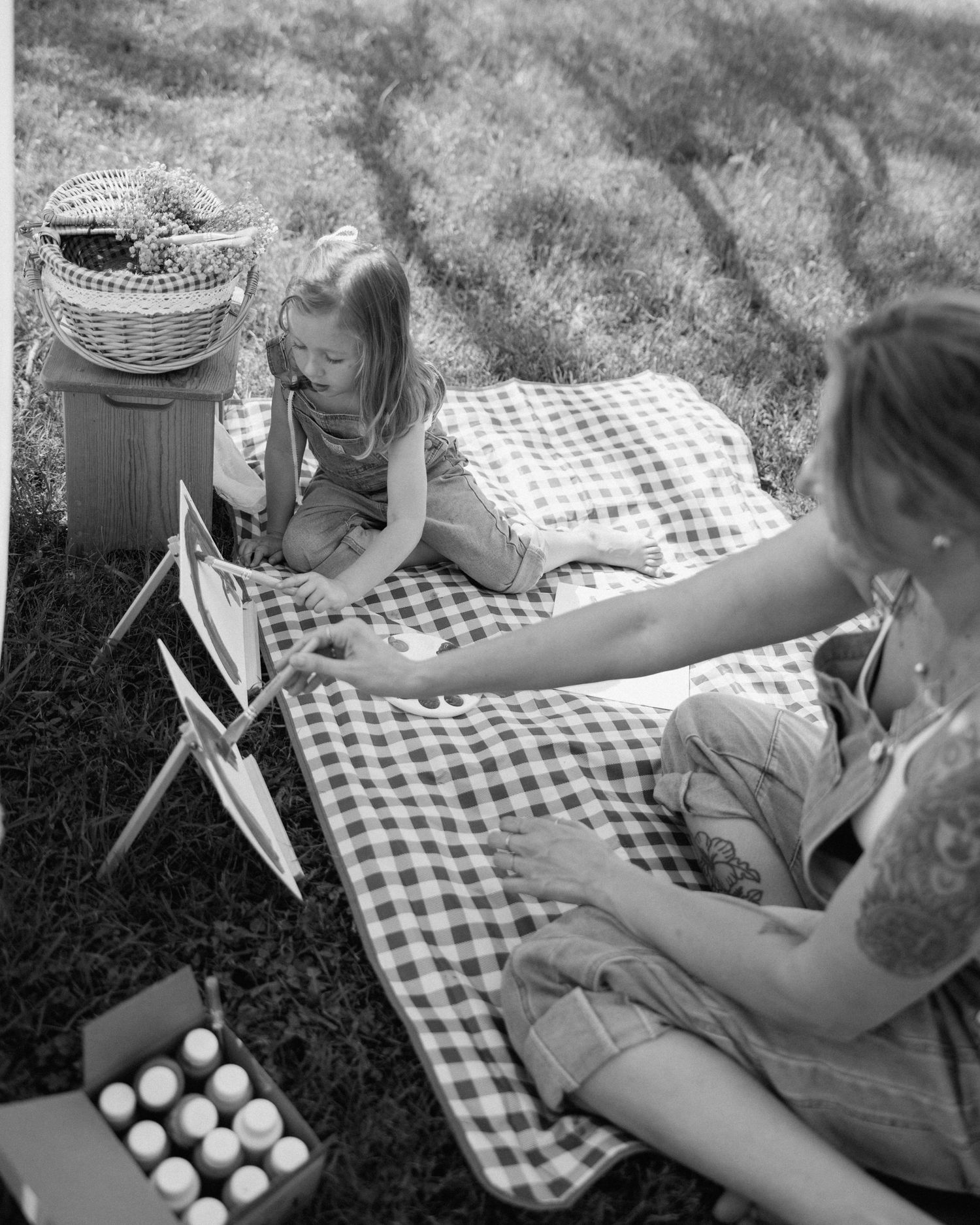 Black and white photo of two children enjoying a picnic on a gingham blanket outdoors with a wicker basket nearby.