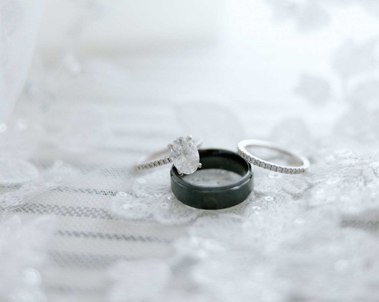 Wedding rings photographed on white lace fabric with black and silver bands.